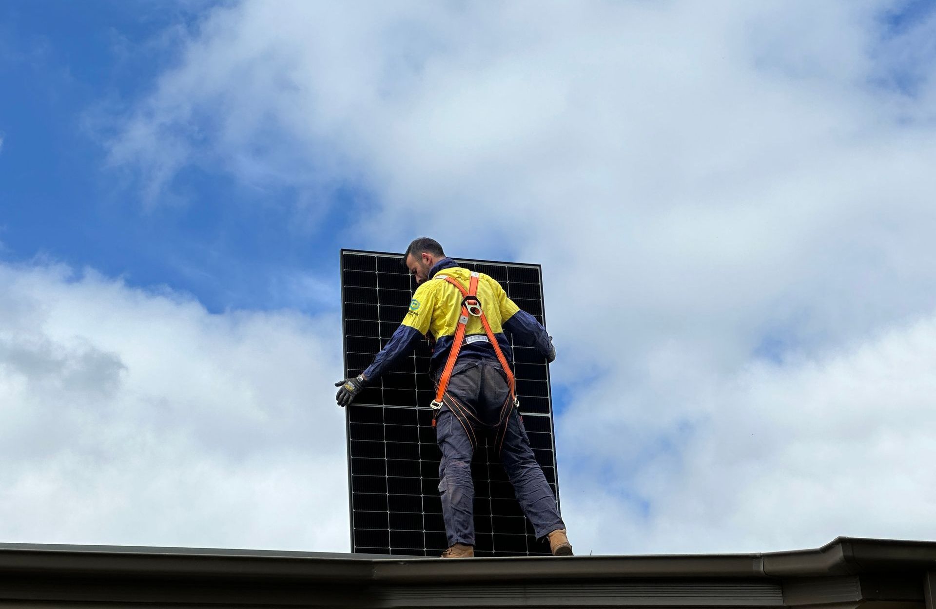 A man is standing on top of a roof holding a solar panel.