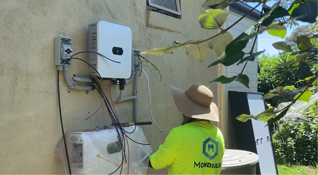 A man in a yellow shirt is working on a solar panel on the side of a building.