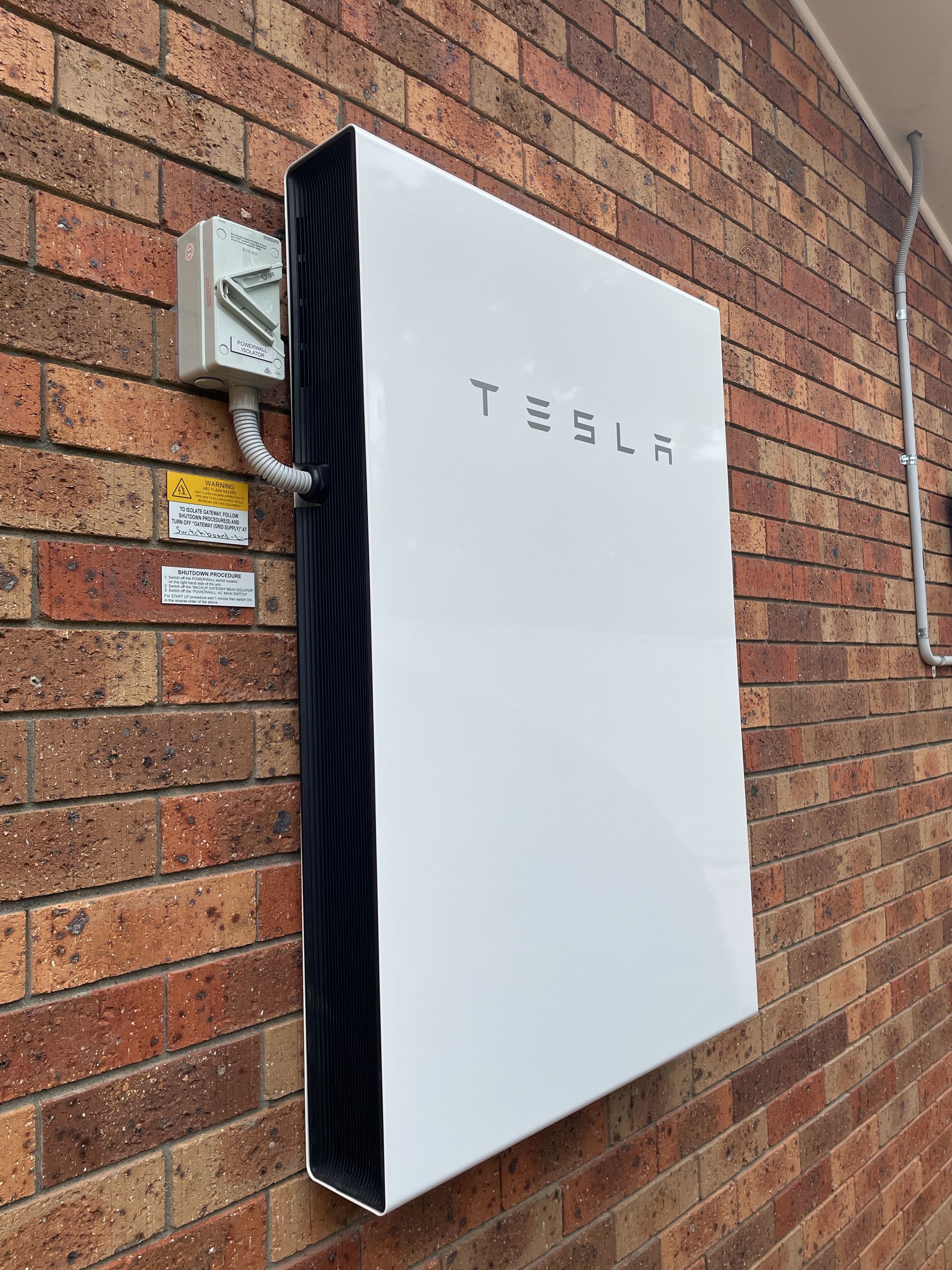 A tesla powerwall is mounted on a brick wall.