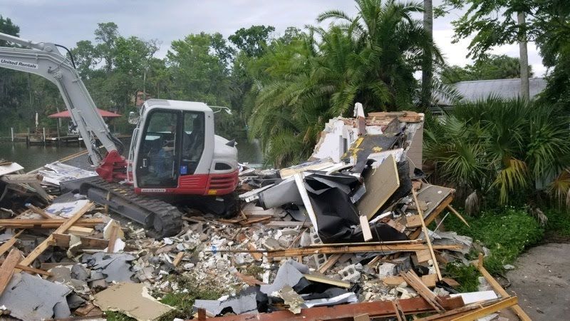 A white and red excavator is demolishing a house