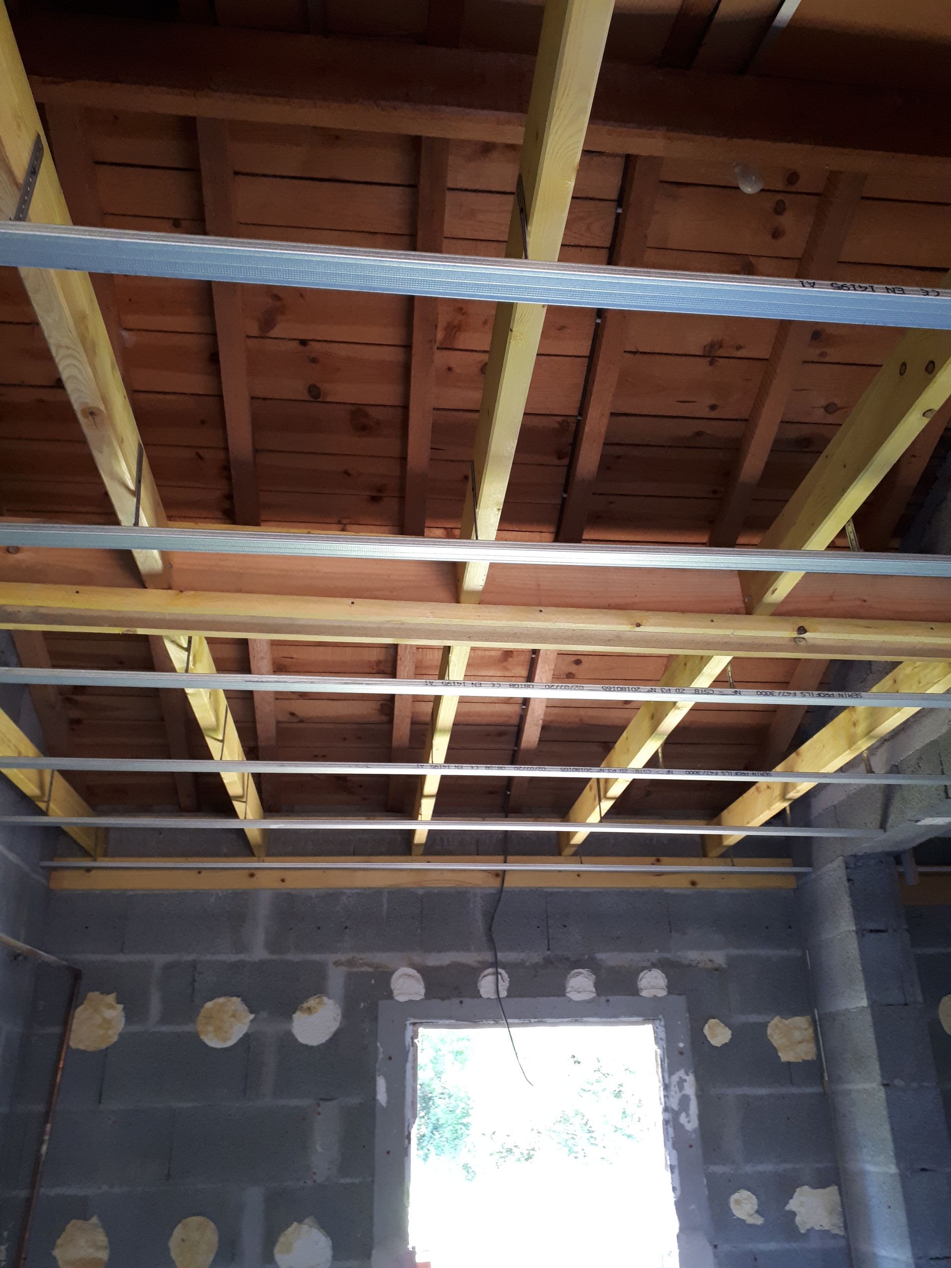 Vue intérieure d'un chantier de construction montrant un plafond à ossature bois avec des supports métalliques