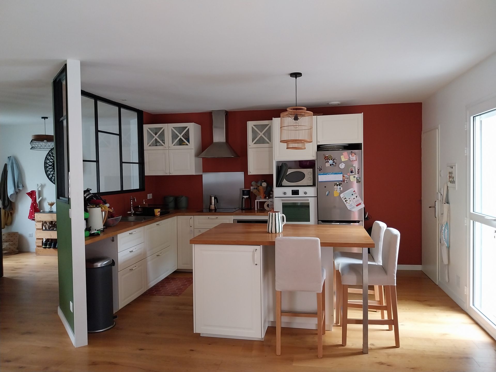 Cuisine avec placards blancs, îlot en bois, mur rouge et coin repas.