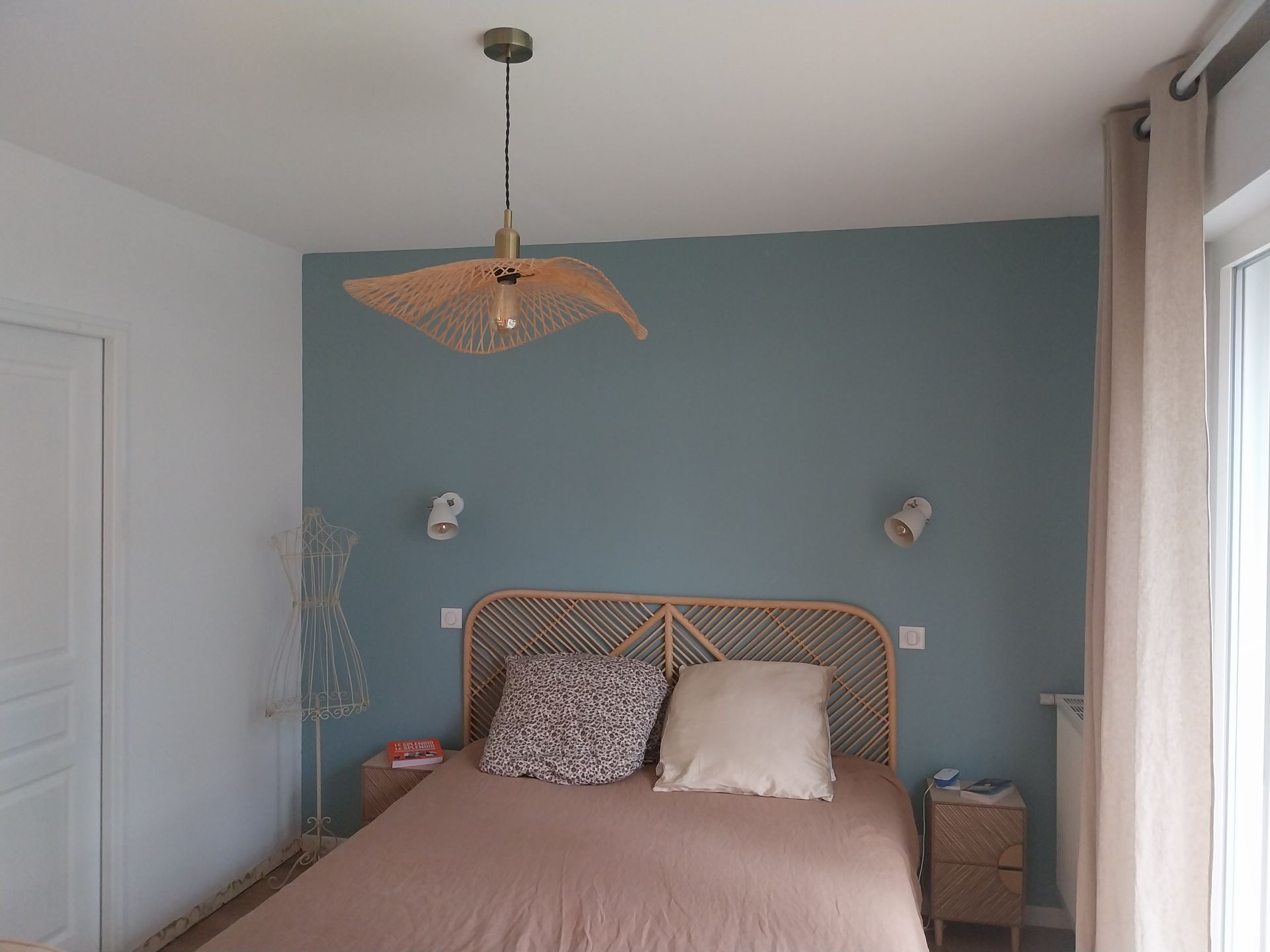 Chambre avec un mur d'accent bleu, une tête de lit en rotin et une suspension lumineuse en osier.