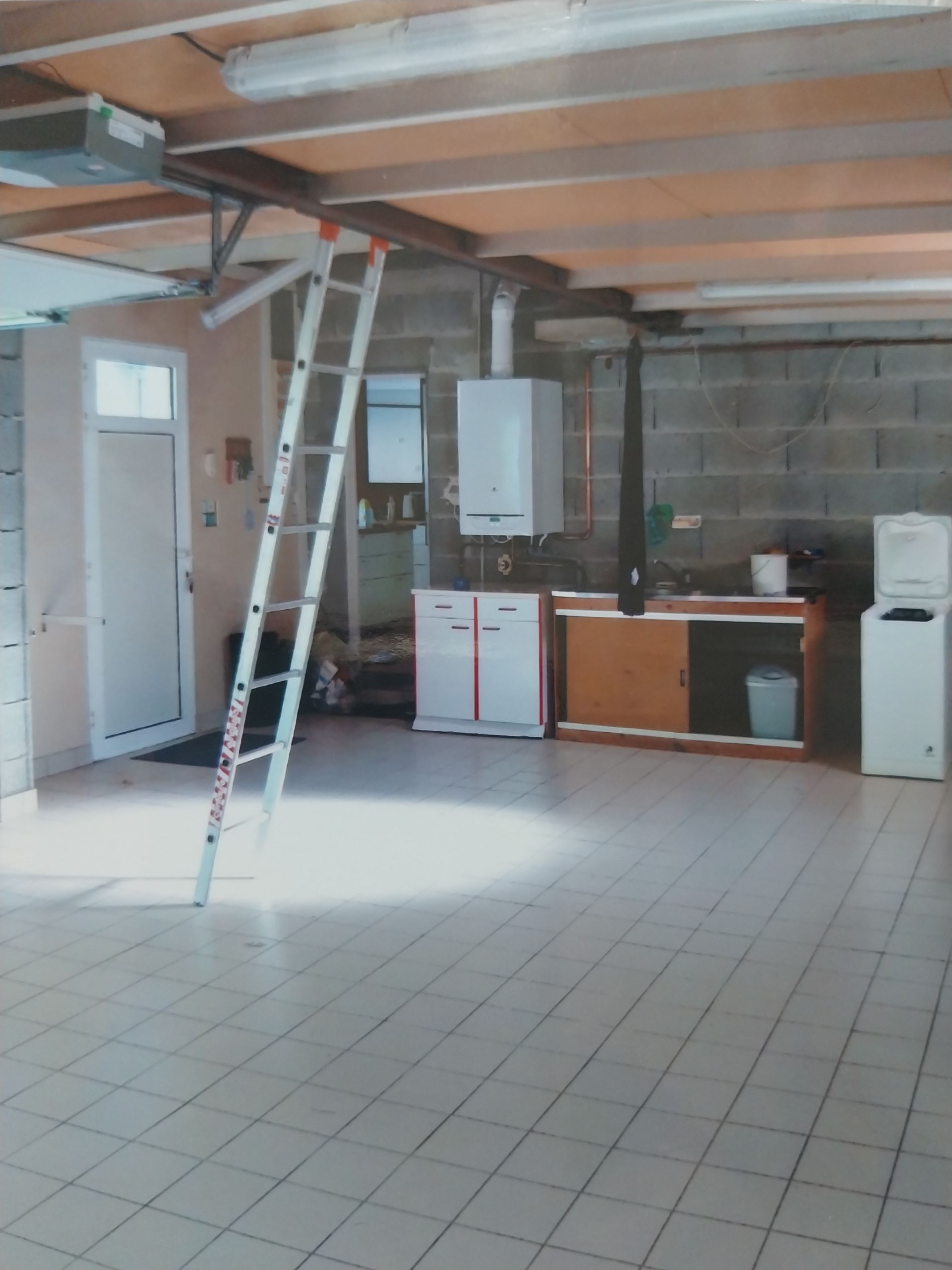 Intérieur du garage avec échelle, appareils électroménagers et poutres en bois apparentes.