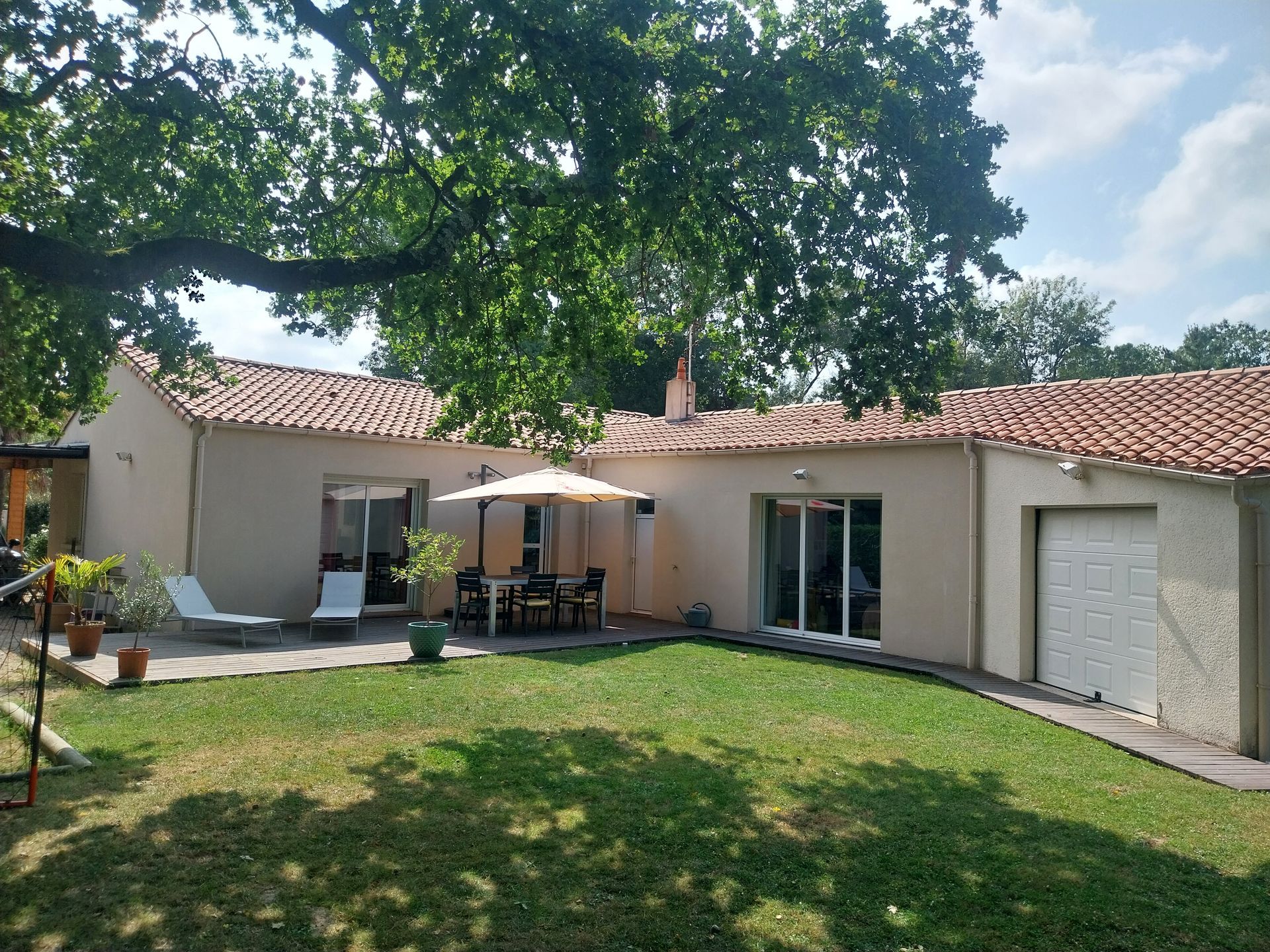 Une maison beige au toit de tuiles orange, un espace repas extérieur et une pelouse verte