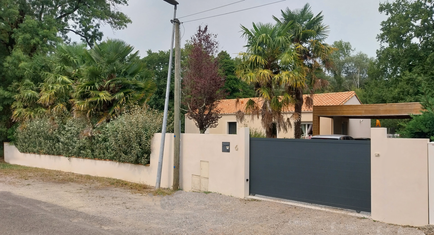 Propriété aux murs beiges avec portail gris foncé, arbres en arrière-plan.