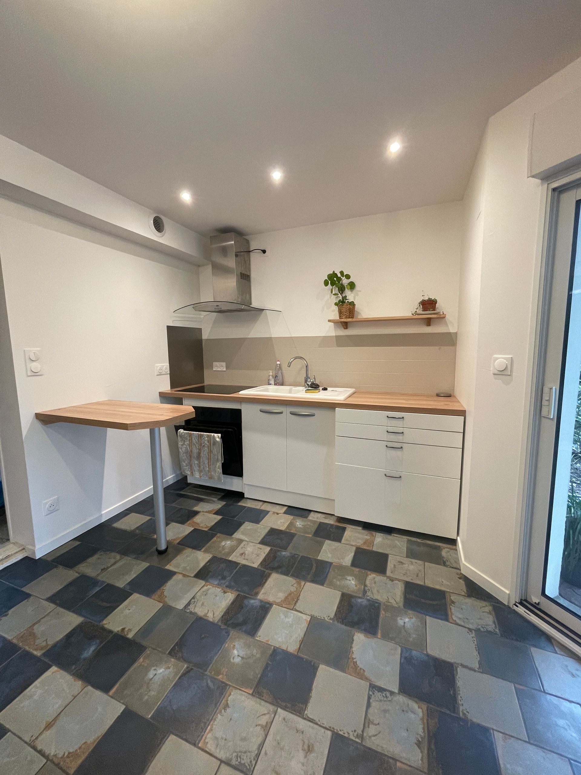 Cuisine avec placards blancs, plan de travail en bois et sol carrelé de carreaux géométriques. Comprend une petite table.