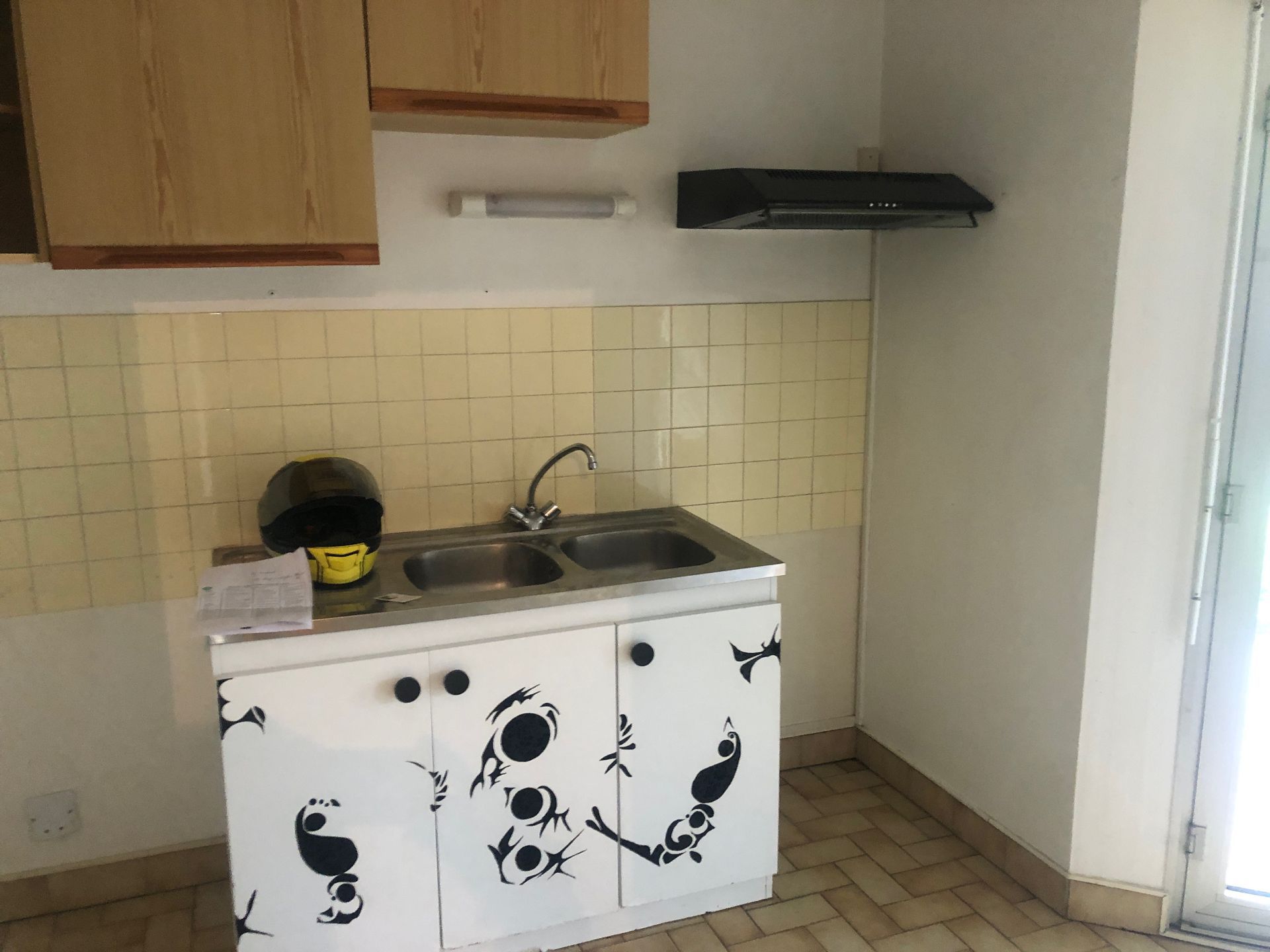 Cuisine avec placards, évier, hotte et crédence carrelée ; un casque repose sur le plan de travail.