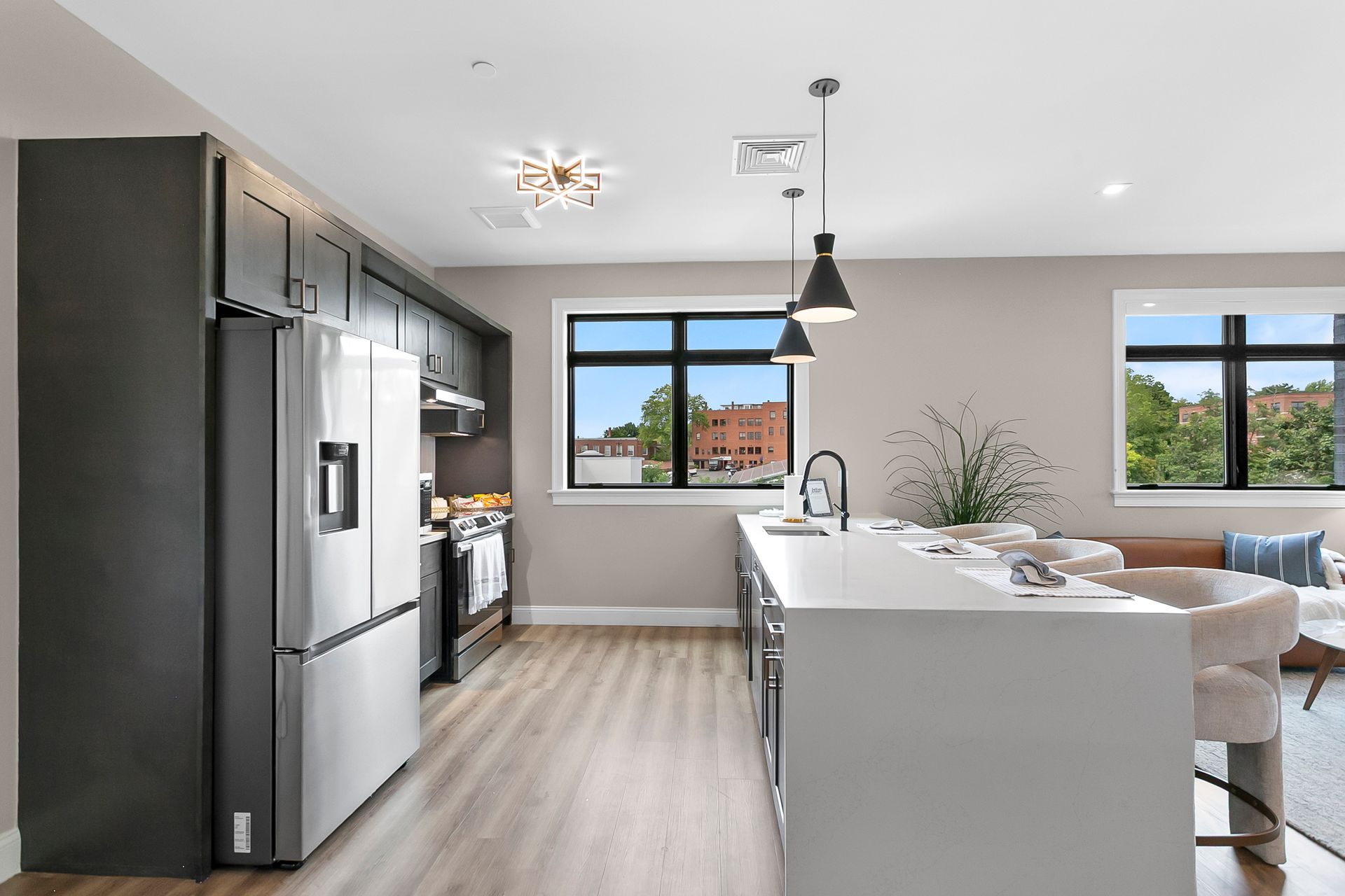 Modern open-plan kitchen with gray appliances, white island, pendant light, and large windows
