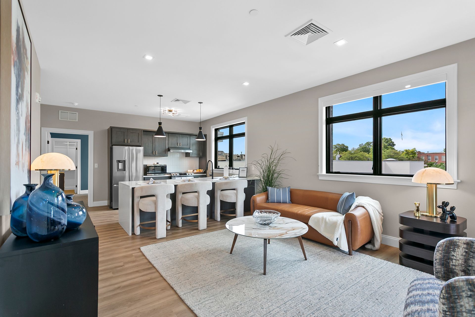 Modern living room with sofa, rug, kitchen island, and large window overlooking greenery