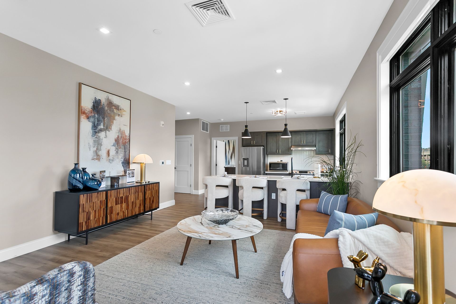 Bright open-concept living room with blue sofa, wood floor, and modern kitchen in back