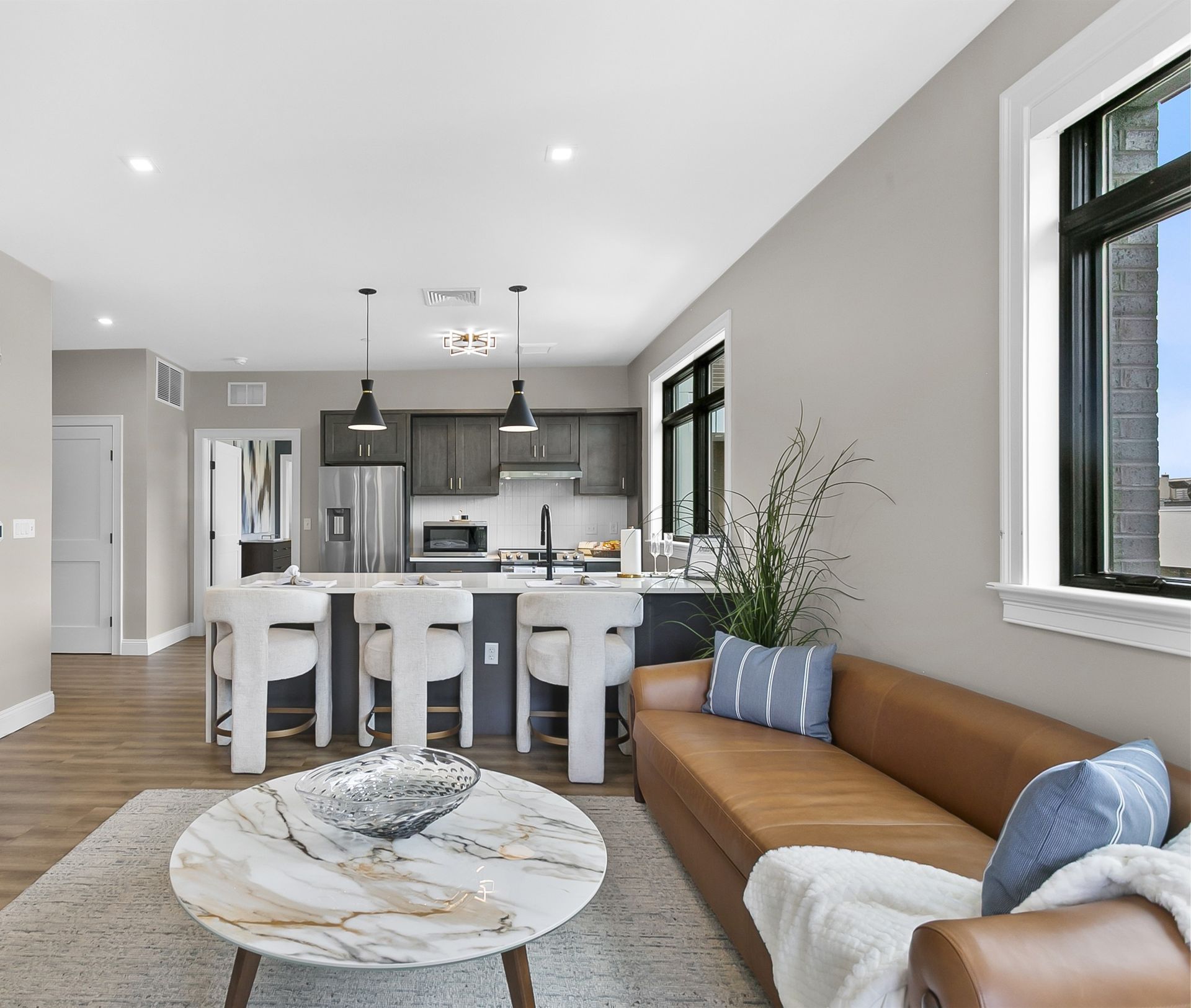Bright open-plan kitchen and living room with tan sofa, marble coffee table, and island seating.