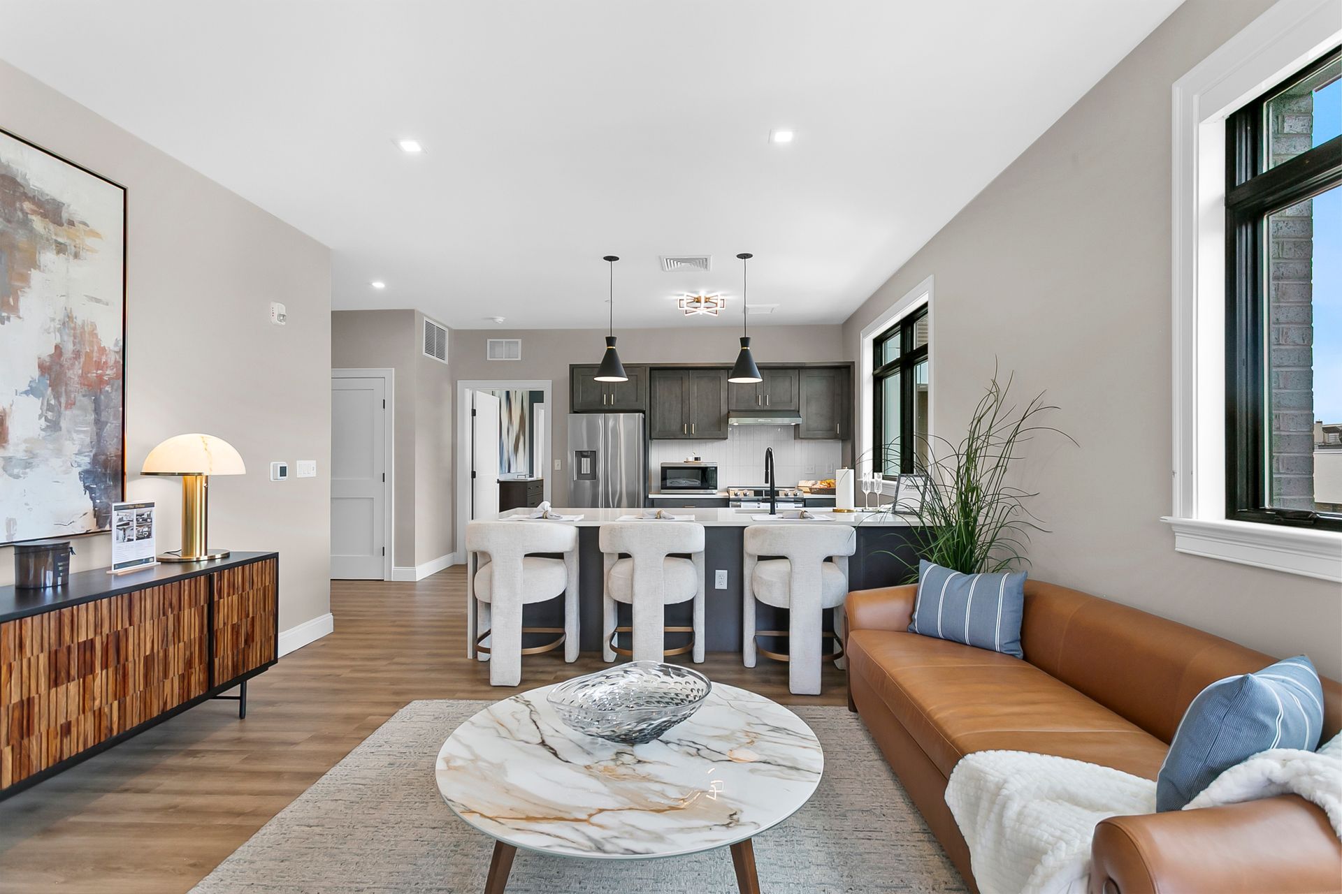 Bright modern living room with tan sofa, round coffee table, and open kitchen with island in the background