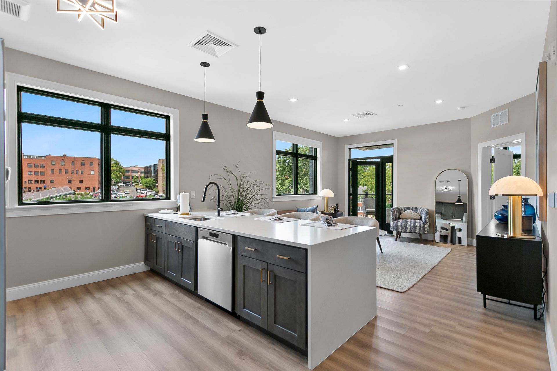 Bright modern kitchen and living area with island, black pendant lights, large windows, and wood floors