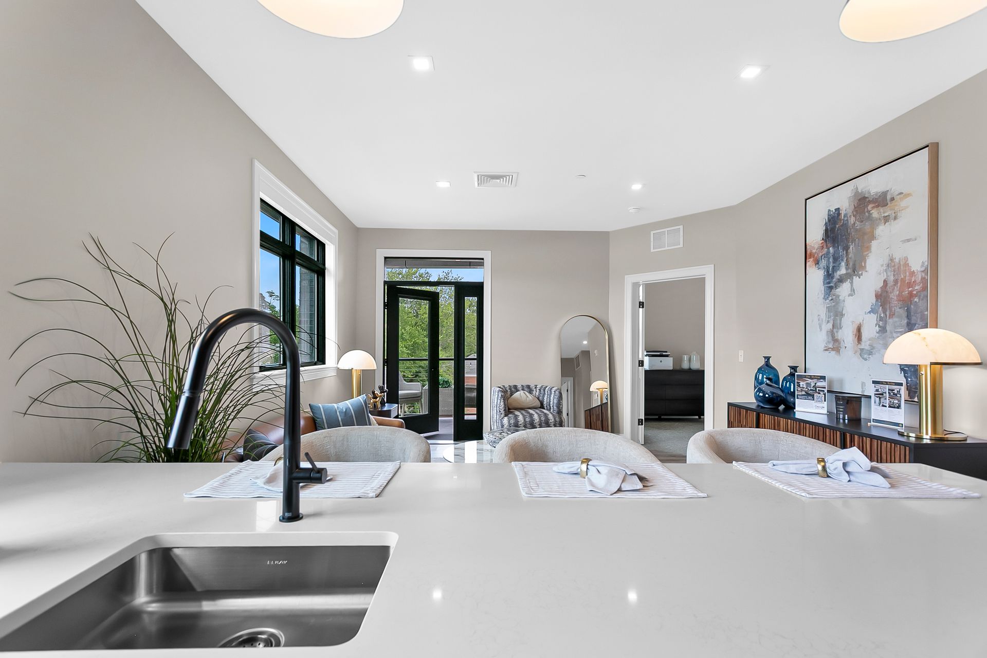 Bright modern bedroom with white bed, large windows, and a sleek sink in the foreground