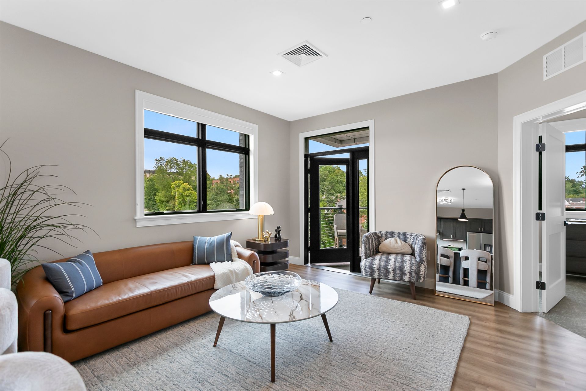 Modern living room with brown sofa, marble coffee table, large windows, and open glass door to balcony
