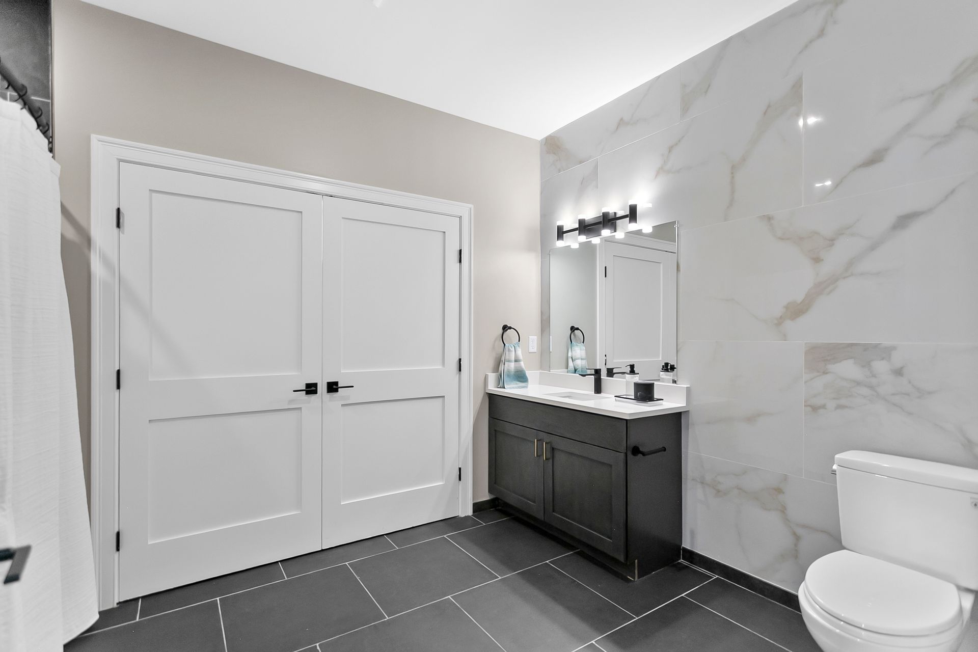 Modern bathroom with double vanity, white marble shower wall, and double doors.
