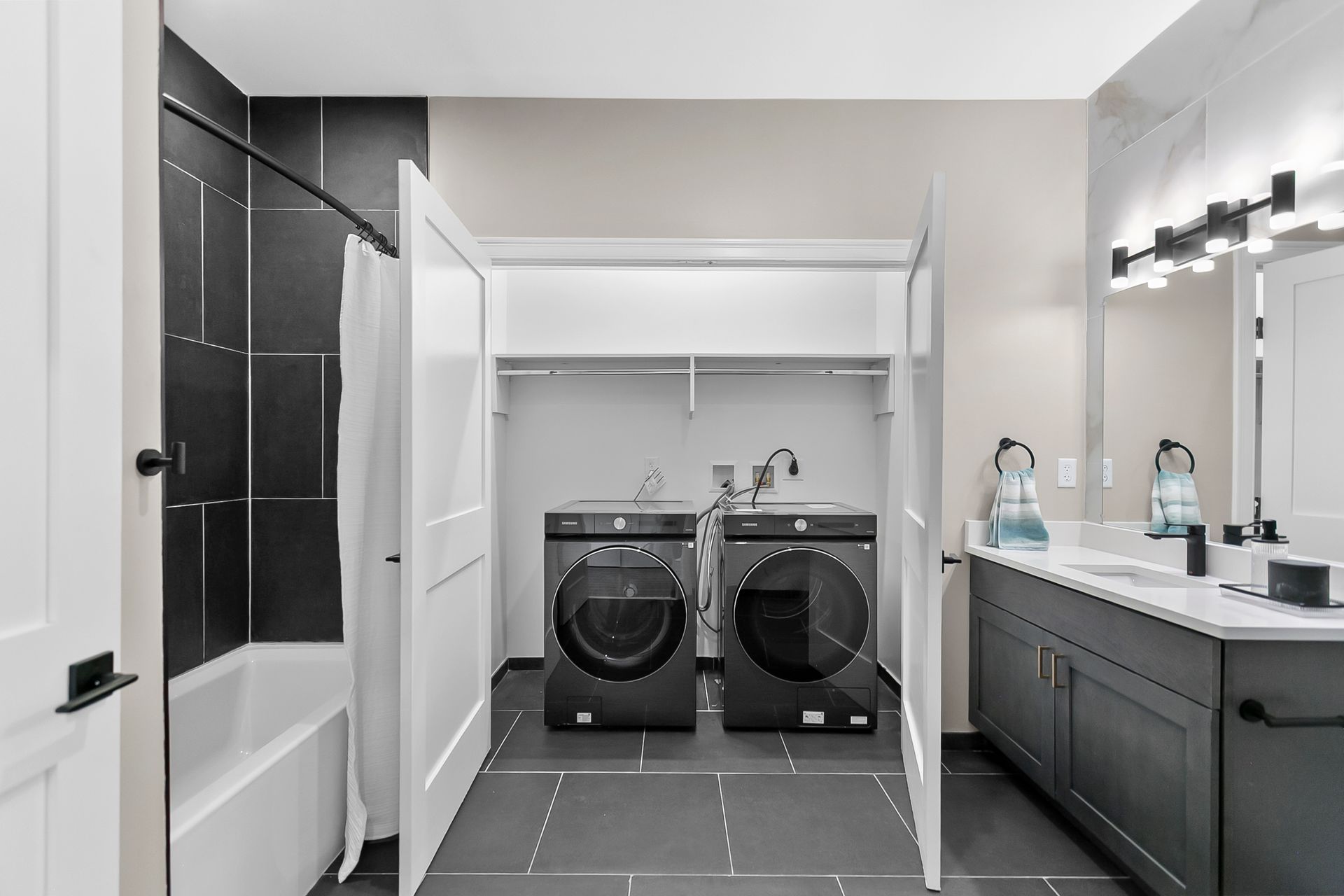 Laundry room with black washer and dryer, white shelving, dark cabinets, and a sink