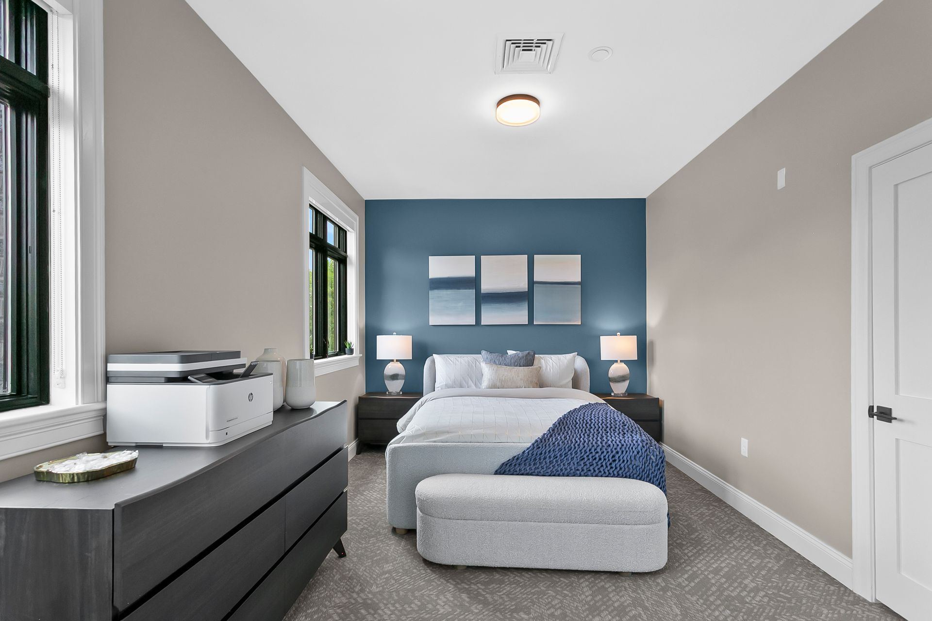 Modern bedroom with blue accent wall, bed, dresser, and carpeted floor
