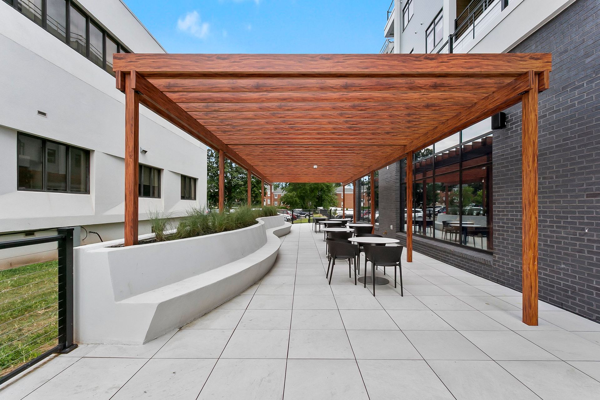 Modern outdoor patio with wooden pergola, white benches, and tables beside a building