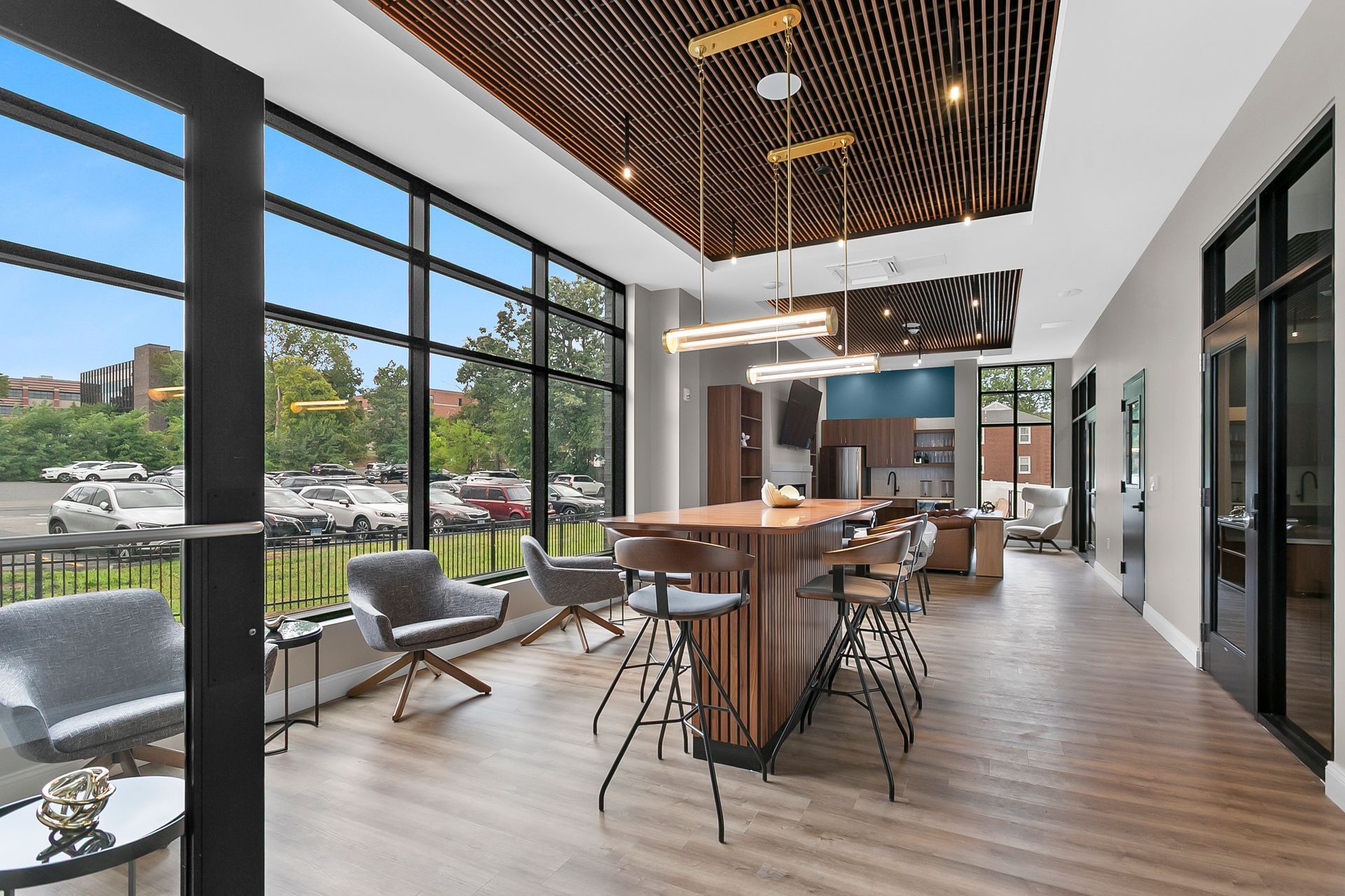 Modern café lounge with wood tables, black chairs, and large windows overlooking a green outdoor area
