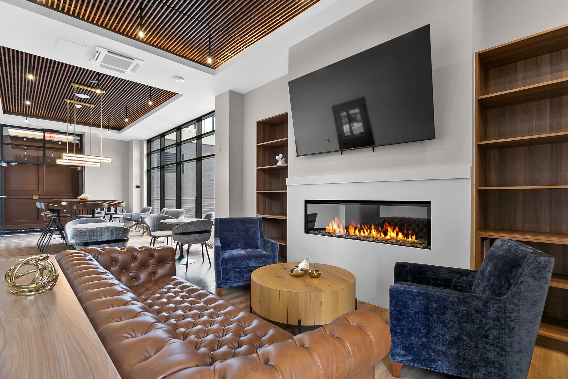 Modern living room with fireplace, wall-mounted TV, blue chairs, and tan leather sofa