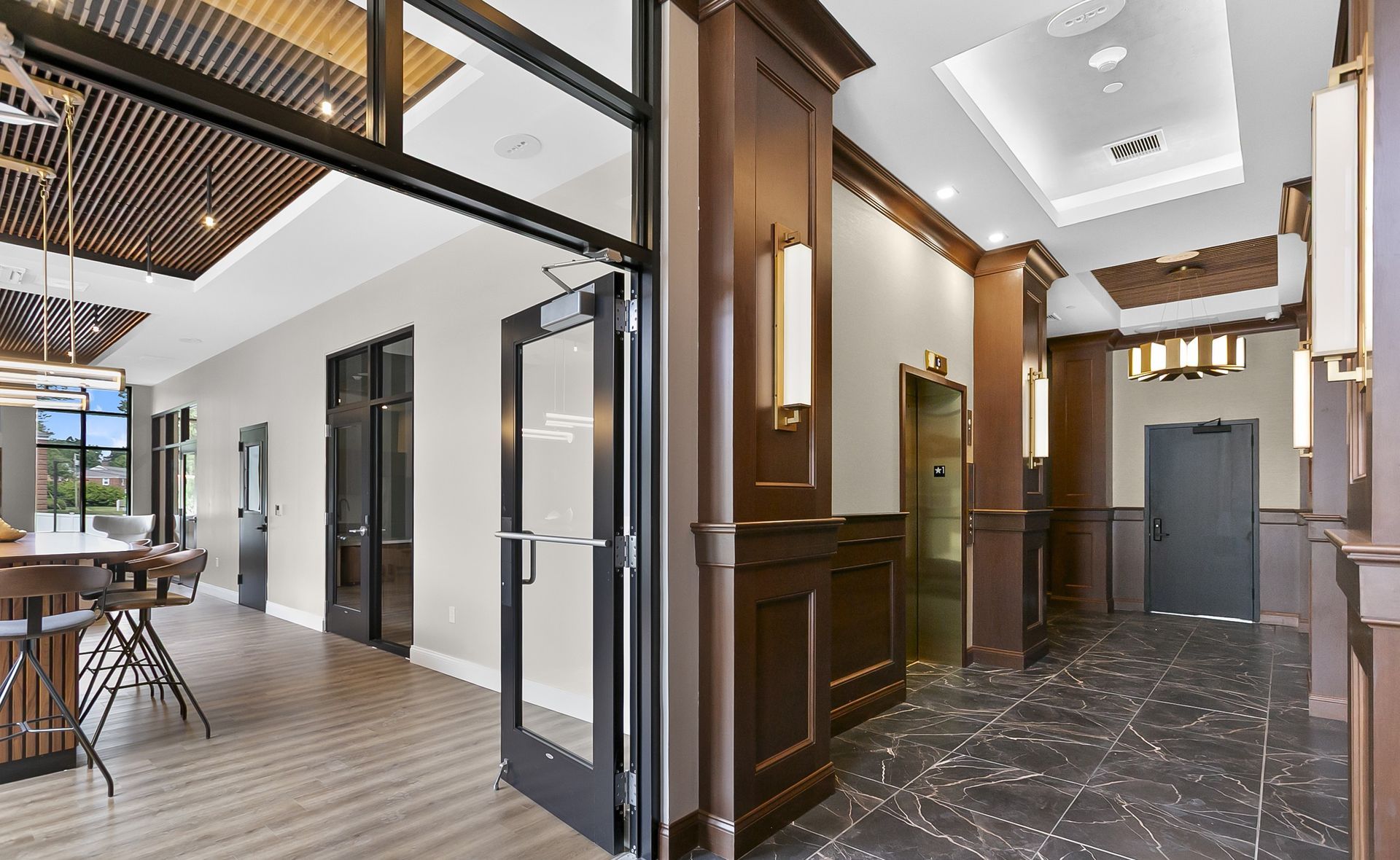 Modern office lobby with wood-paneled walls, black marble floor, and glass doors leading to a bright open workspace