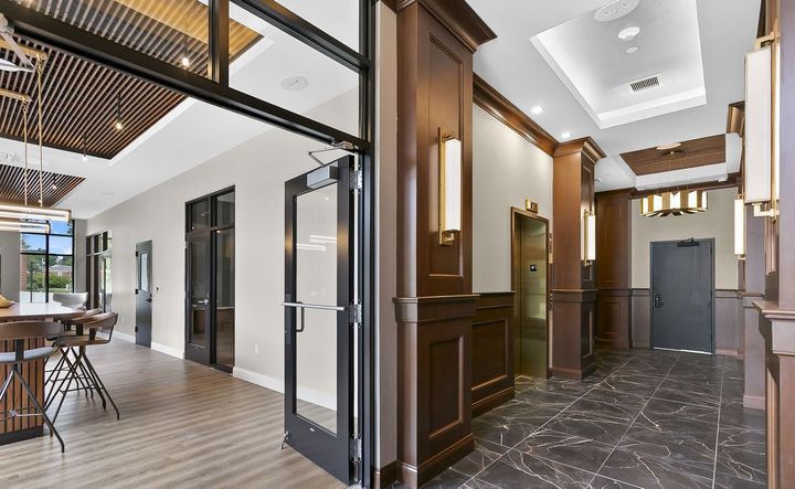Modern office lobby with wood-paneled walls, black marble floor, and glass doors leading to a bright open workspace