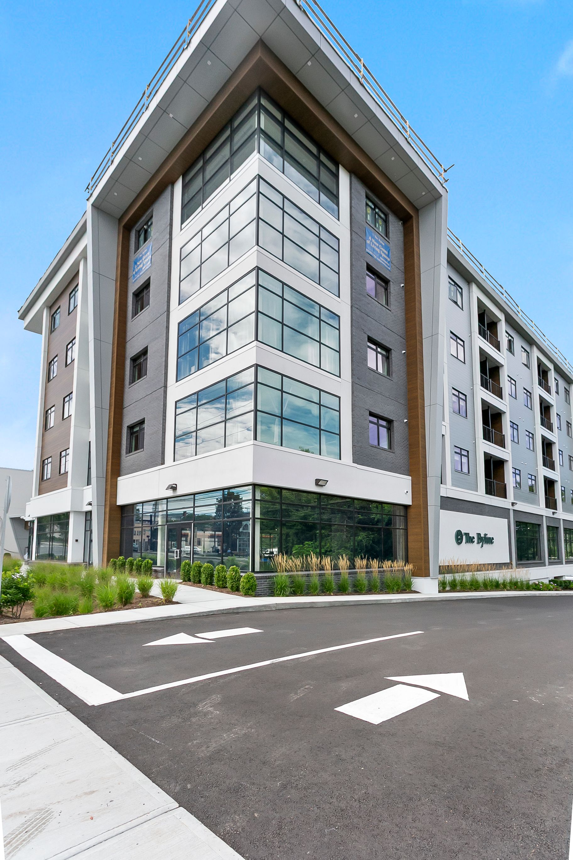 Modern multi-story apartment building with glass balconies and a parking lot under a blue sky