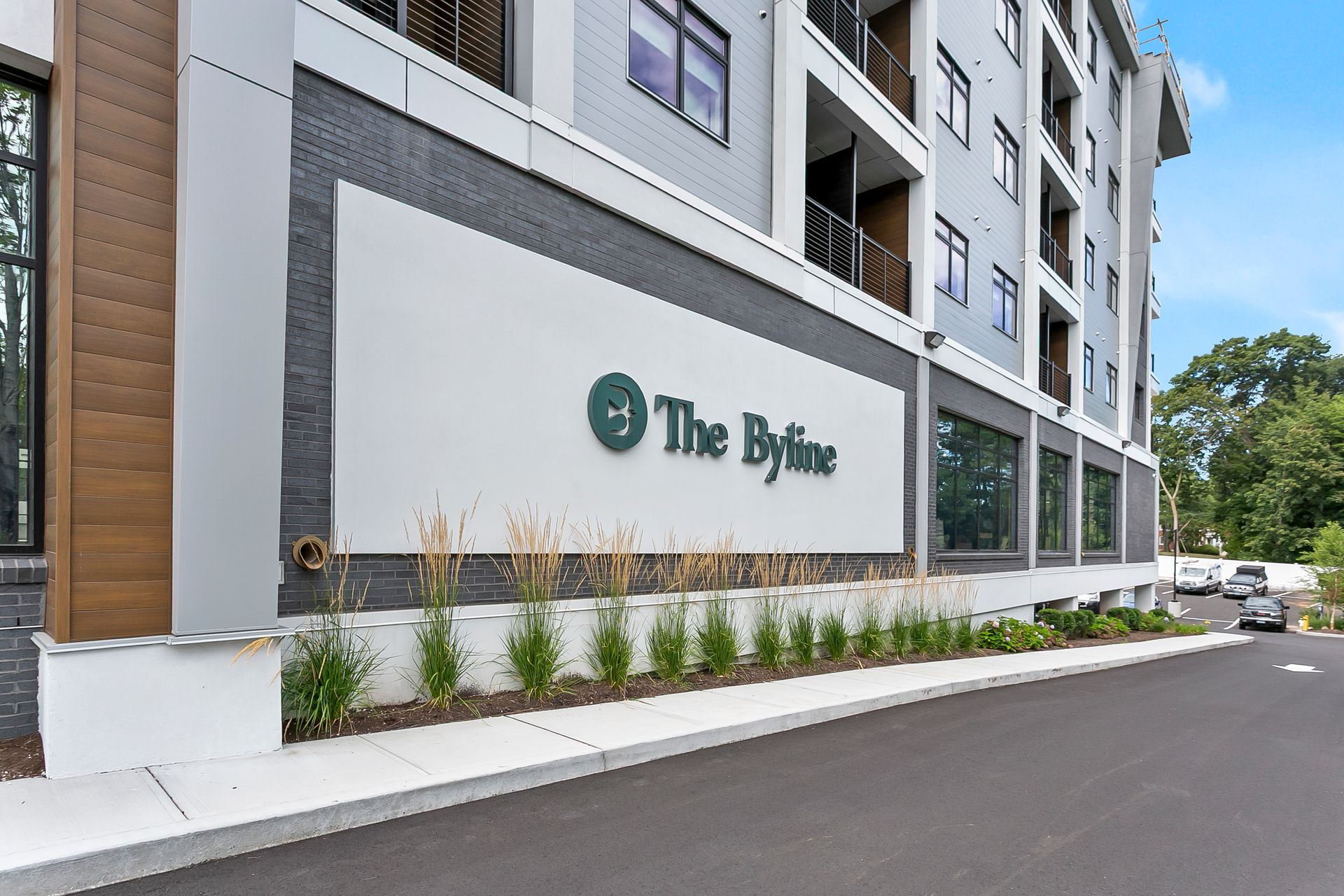 Exterior of The Bryne apartment building with a white sign, gray facade, and landscaped walkway