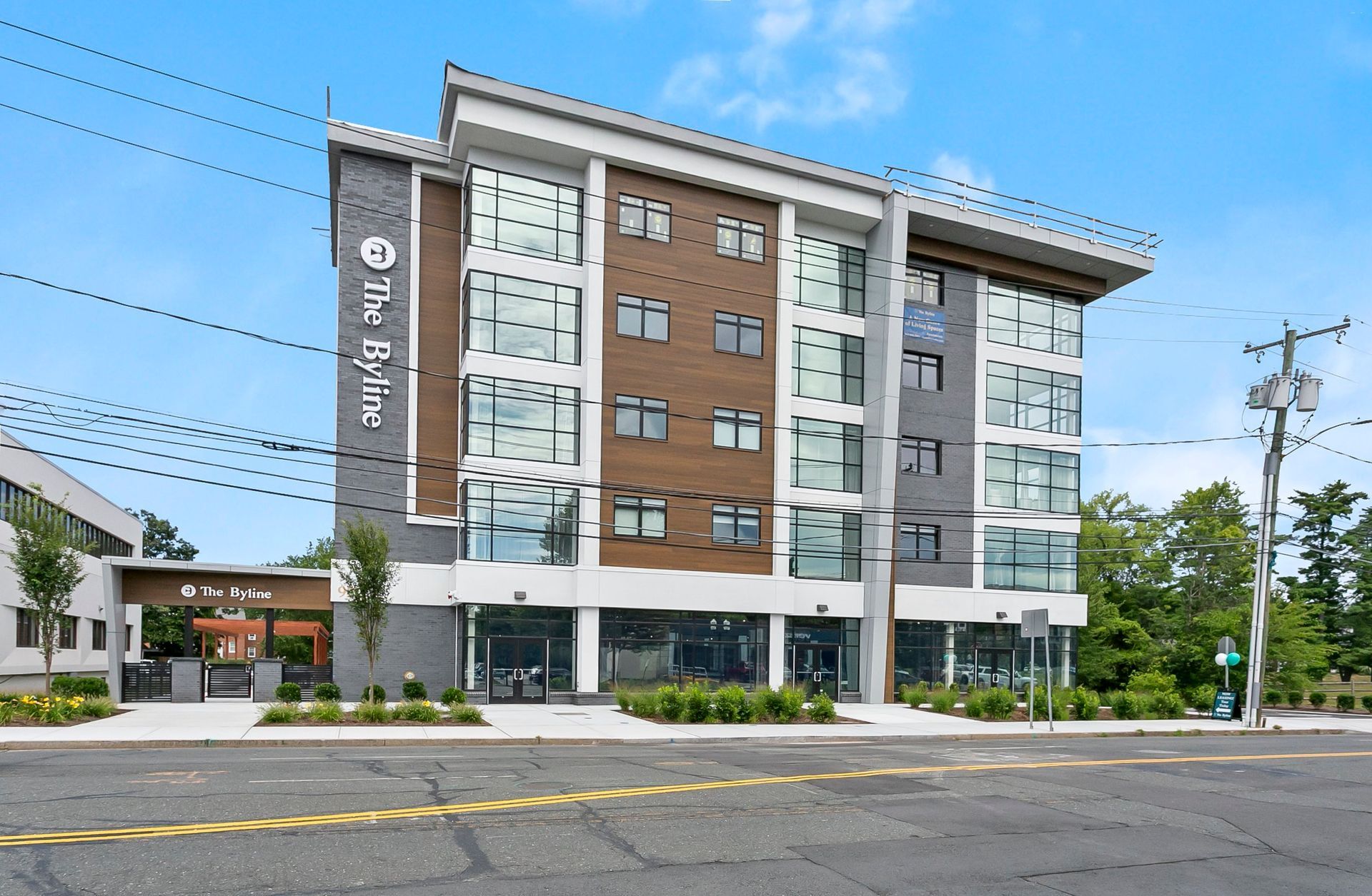 Modern five-story hotel with white and brown facade on a sunny street corner.