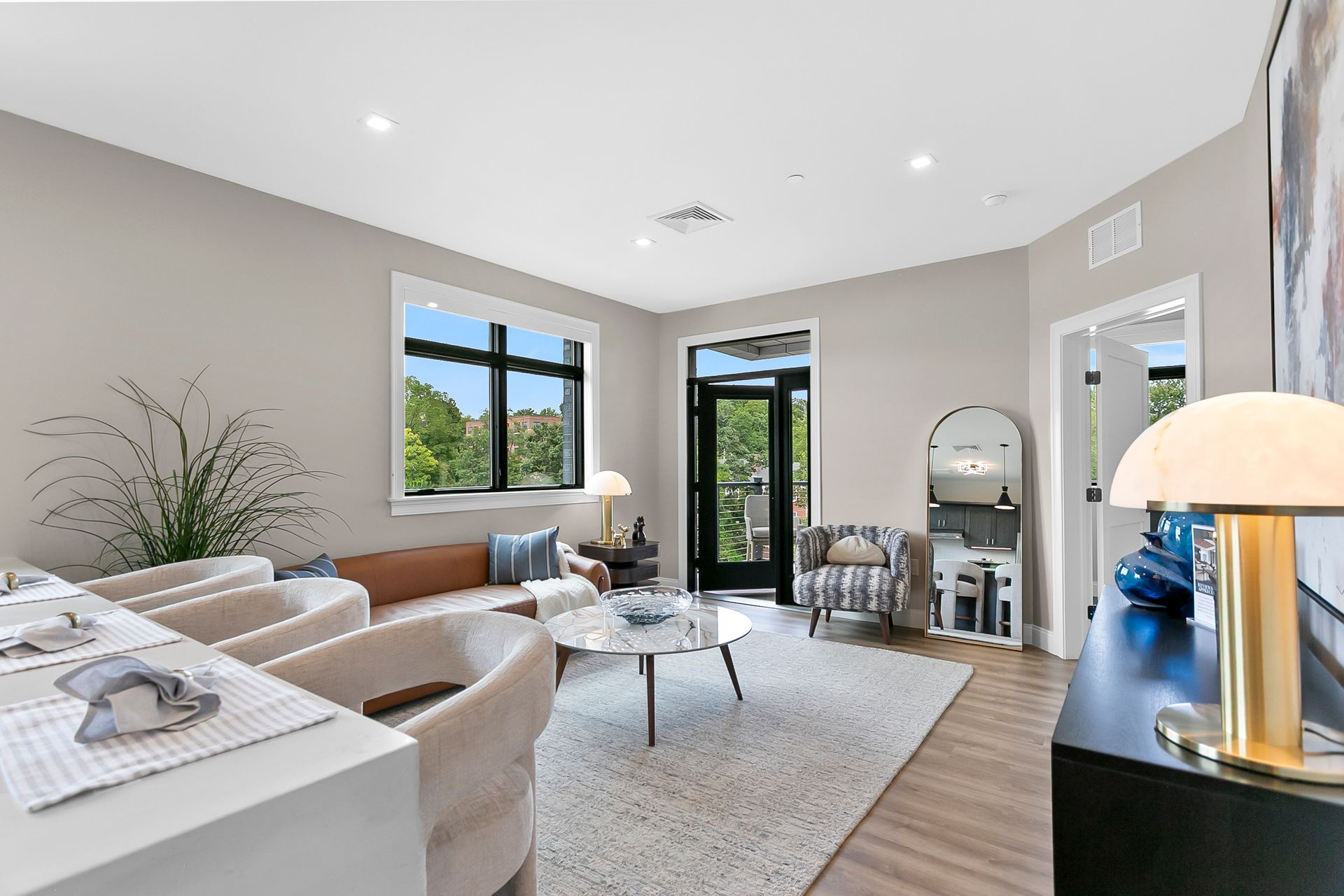 Bright modern living room with beige sectional, coffee table, large windows, and a glass door to outside.