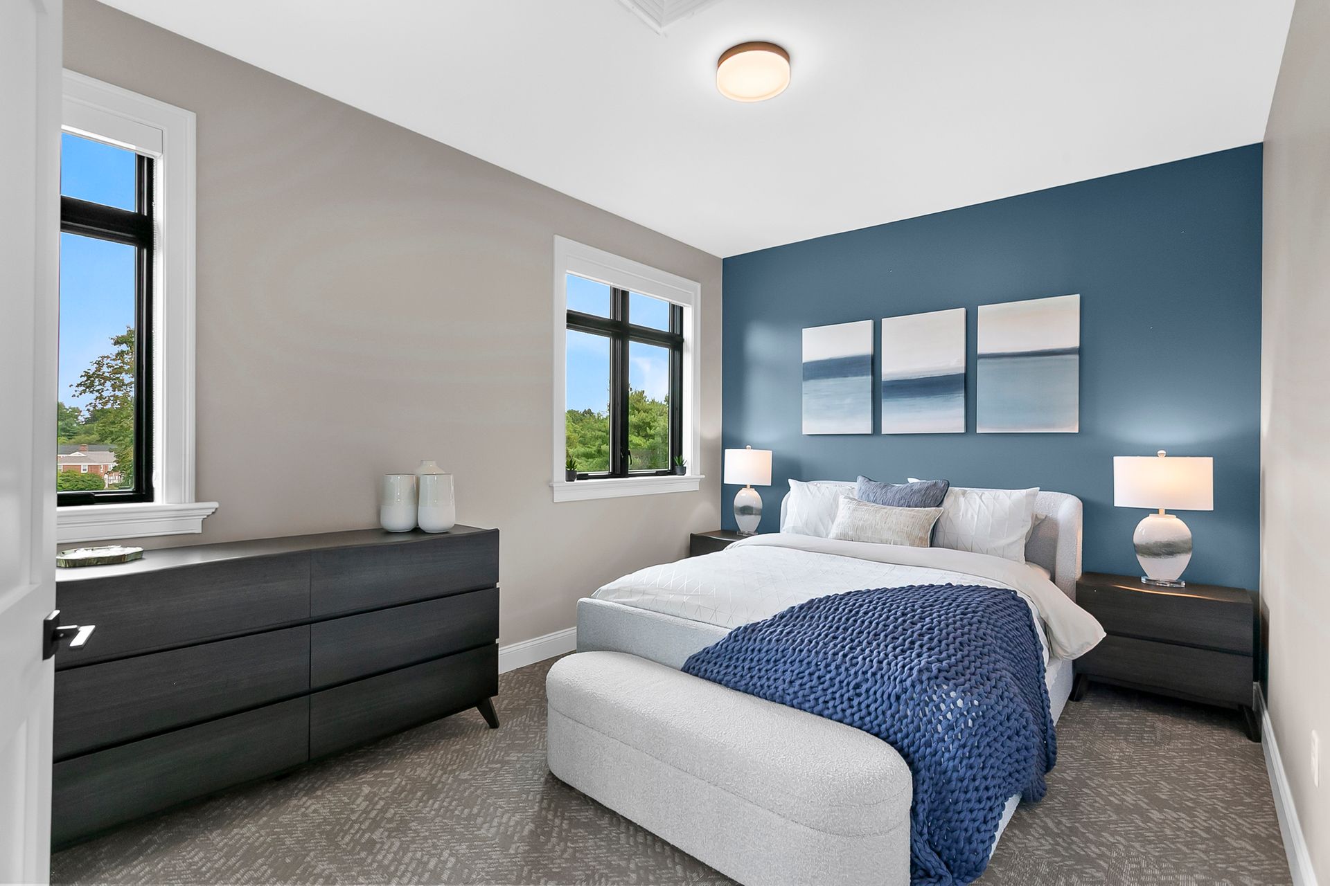 Modern bedroom with blue accent wall, white bed, two windows, and dark dresser