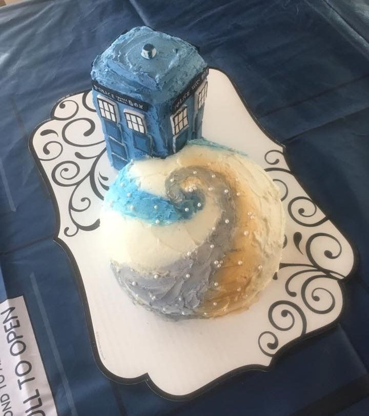 Cake decorated as the Tardis on a planet with swirling blue, gold, and white frosting.