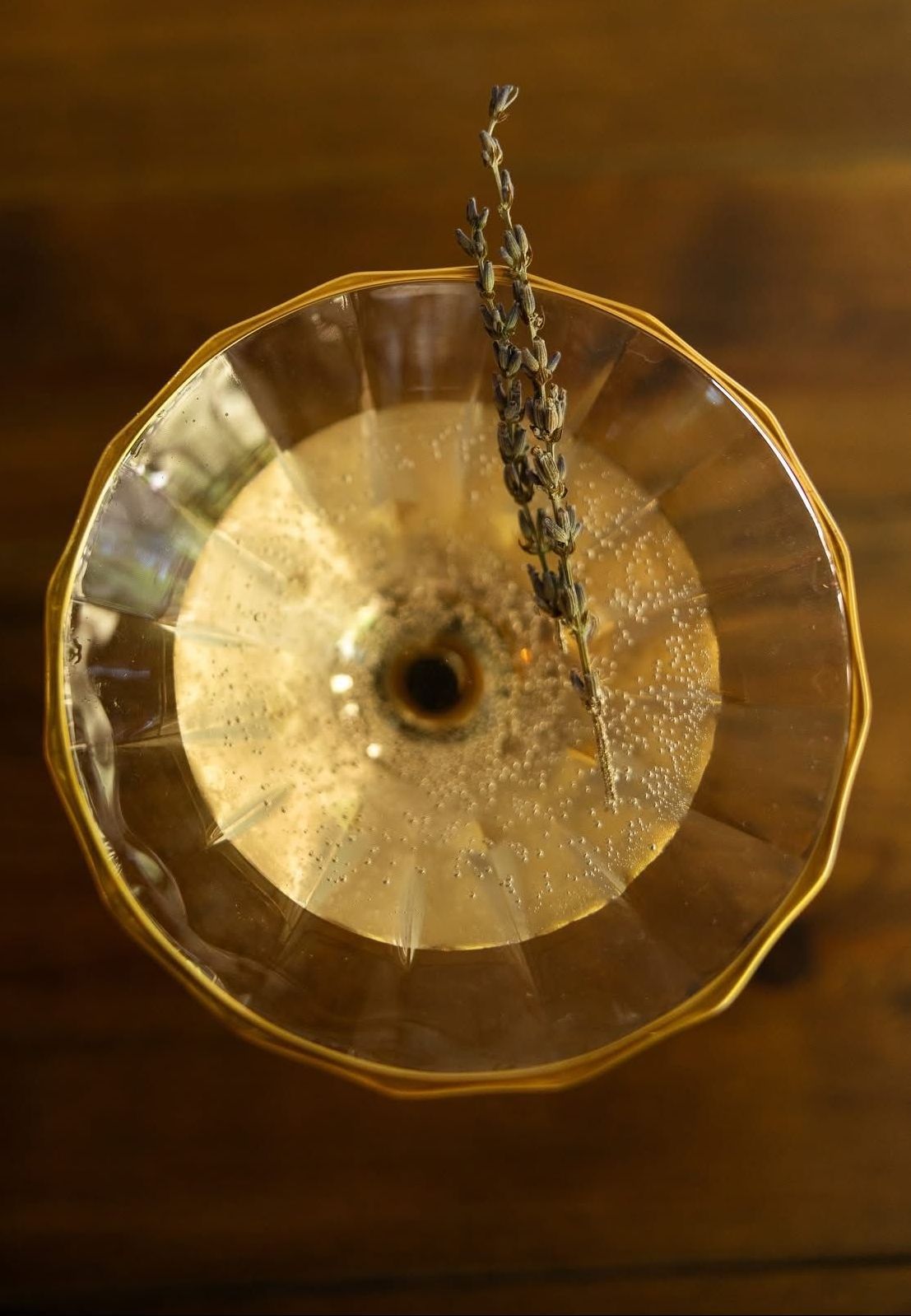 Cocktail in a decorative glass with a sprig of lavender on a wooden surface.