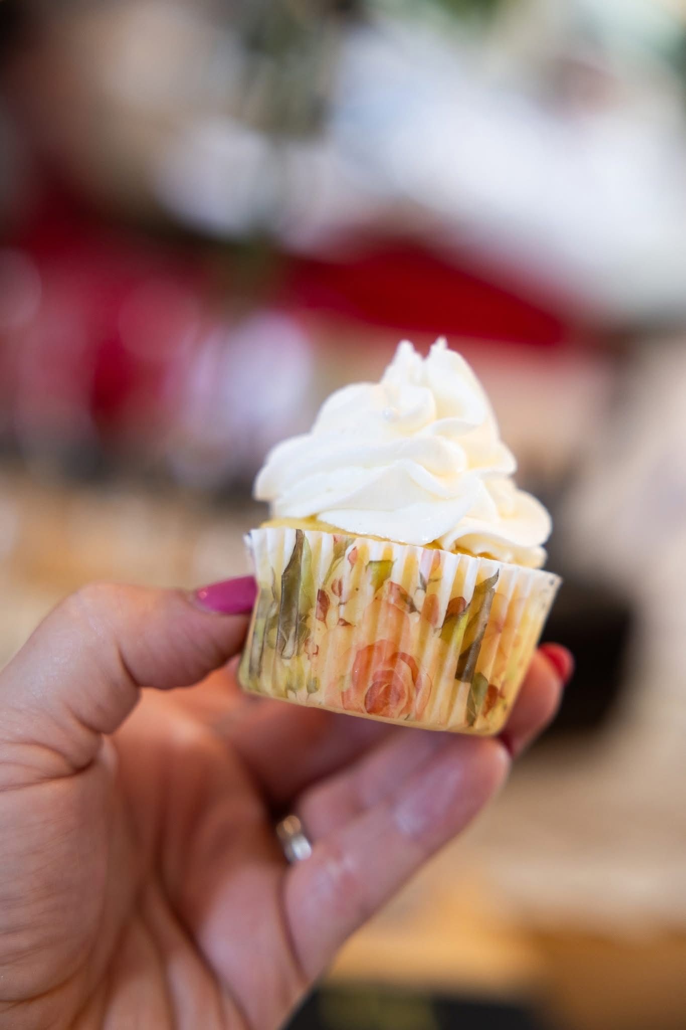 Hand holding a cupcake with white frosting, inside a decorative liner.