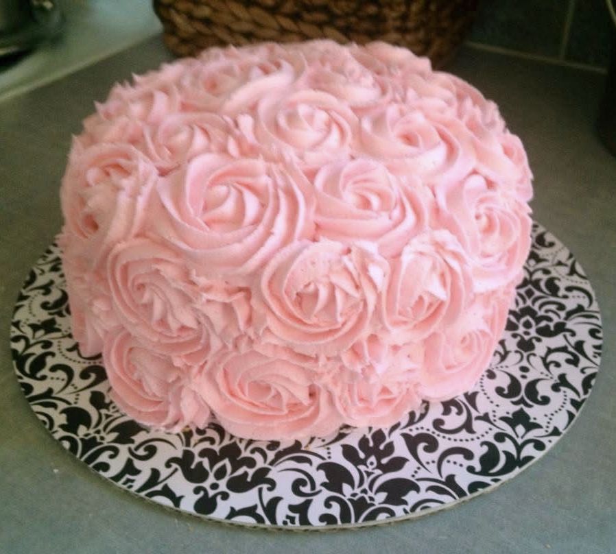 Pink rose-covered cake on a black and white patterned plate, set on a kitchen counter.