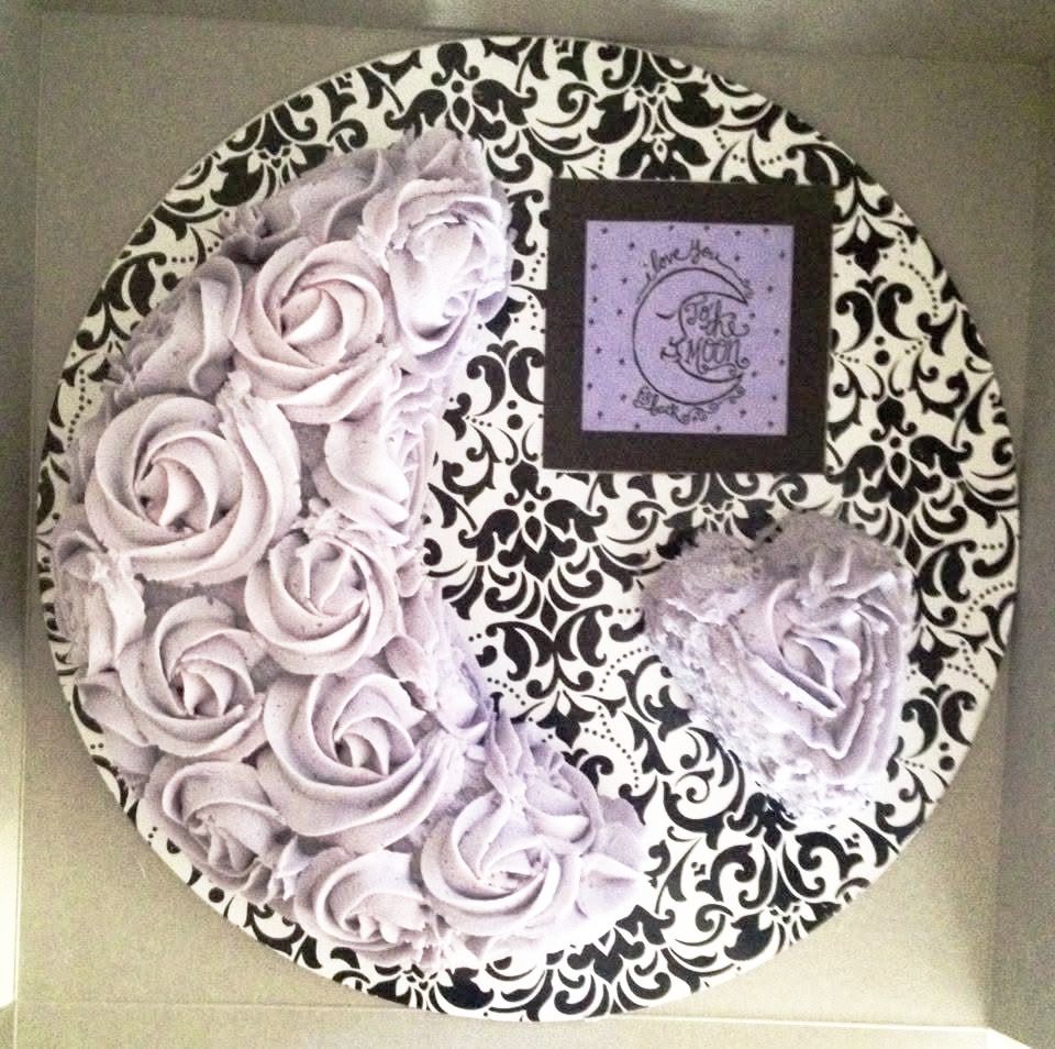 Cake decorated with purple rosettes and a heart on a black and white patterned plate.