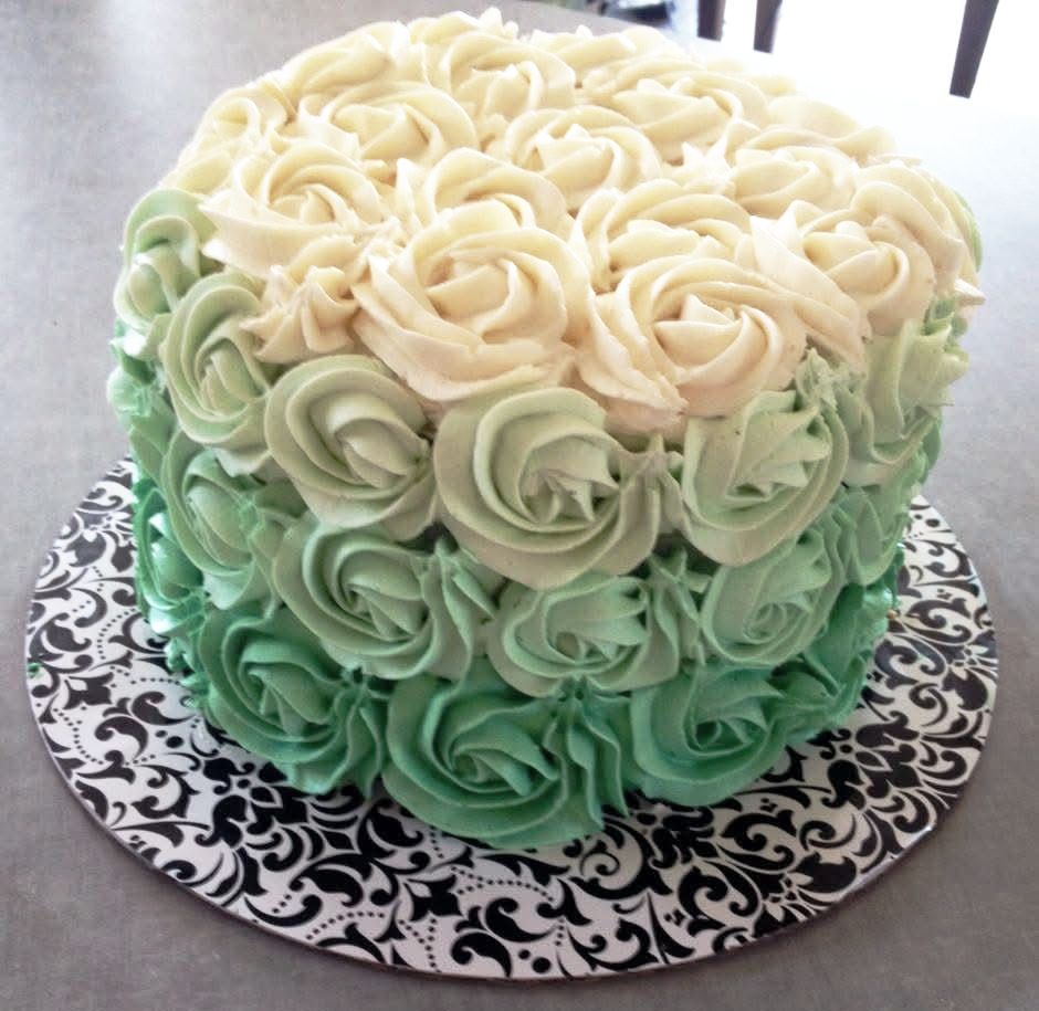 Cake decorated with buttercream roses, ombre effect from green to white, on a patterned cake stand.