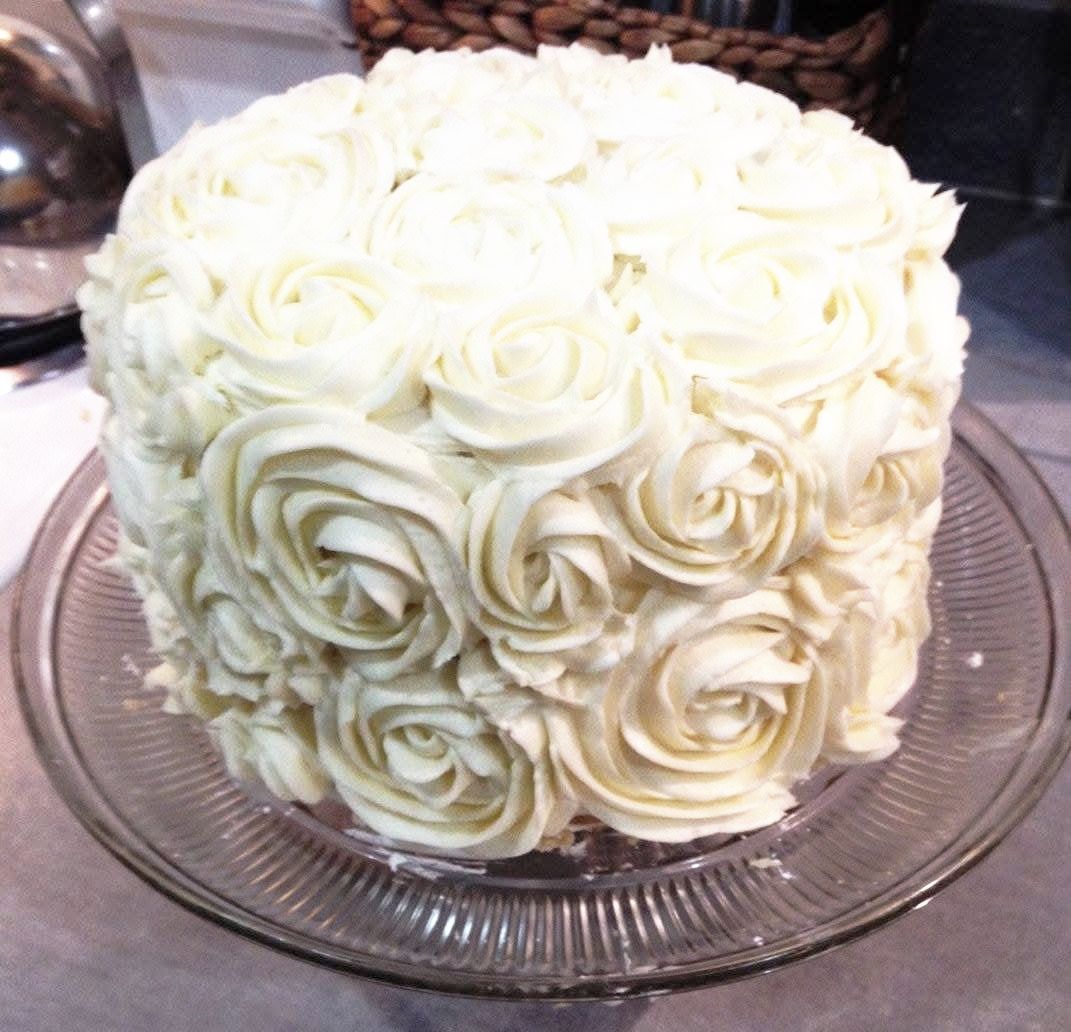 White frosted cake decorated with buttercream roses on a glass cake stand.