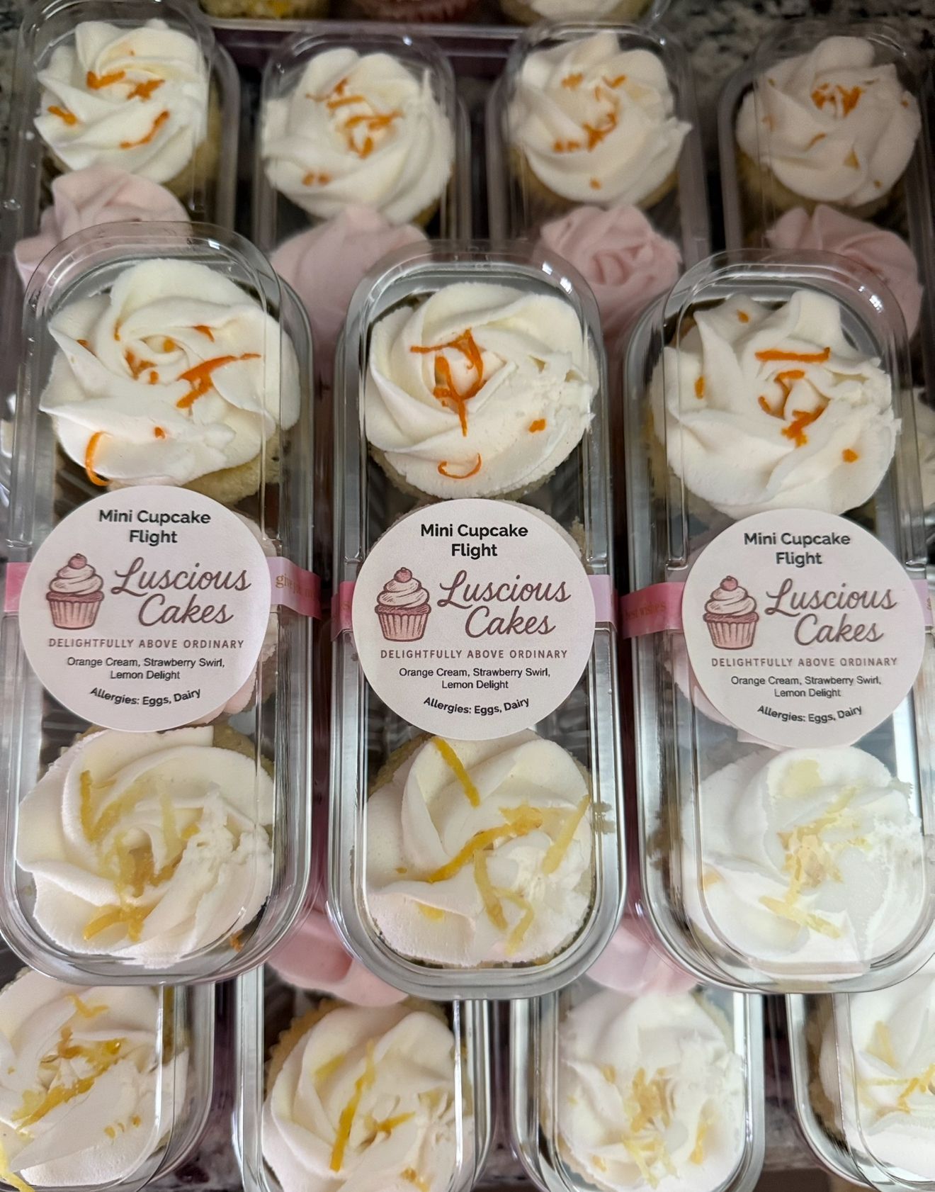 Mini cupcake flight containers with white frosting, lemon zest, and orange accents. 