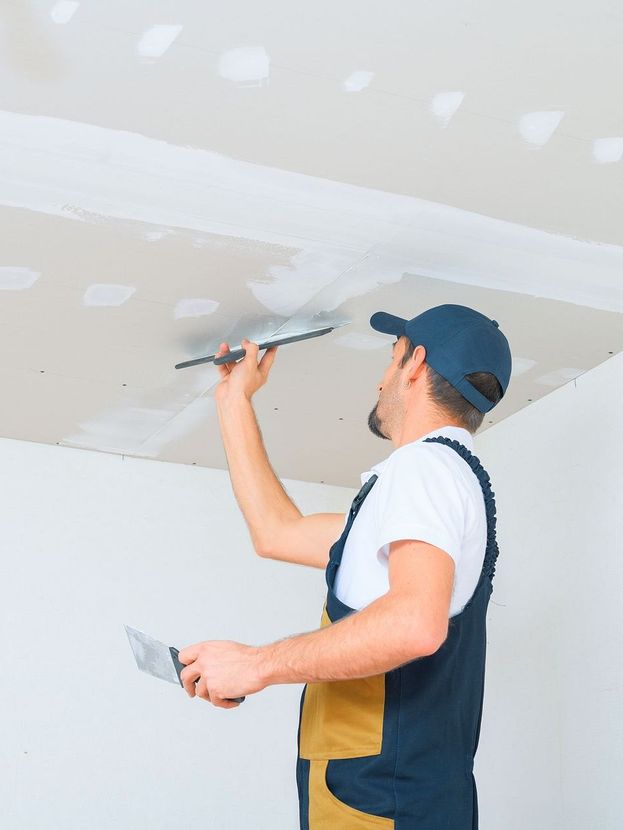 A man is plastering a ceiling with a spatula.