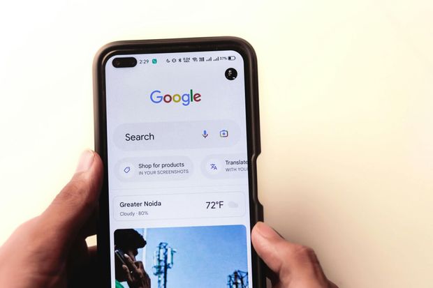 A person is holding a cell phone with the google search page open.
