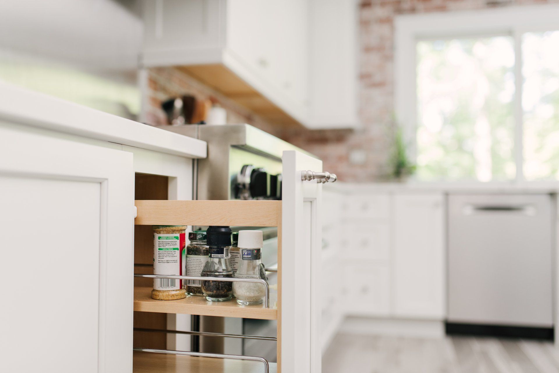 A kitchen with white cabinets and a pull out spice rack.
