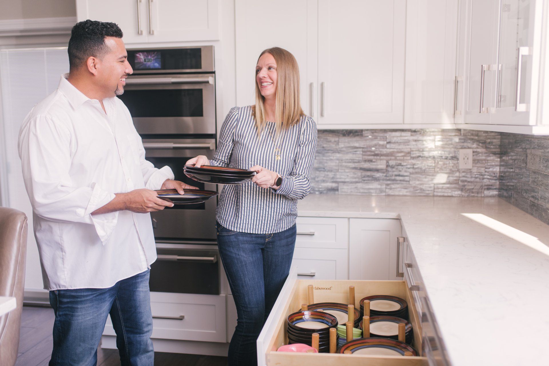 A man and a woman are standing in a kitchen holding plates.