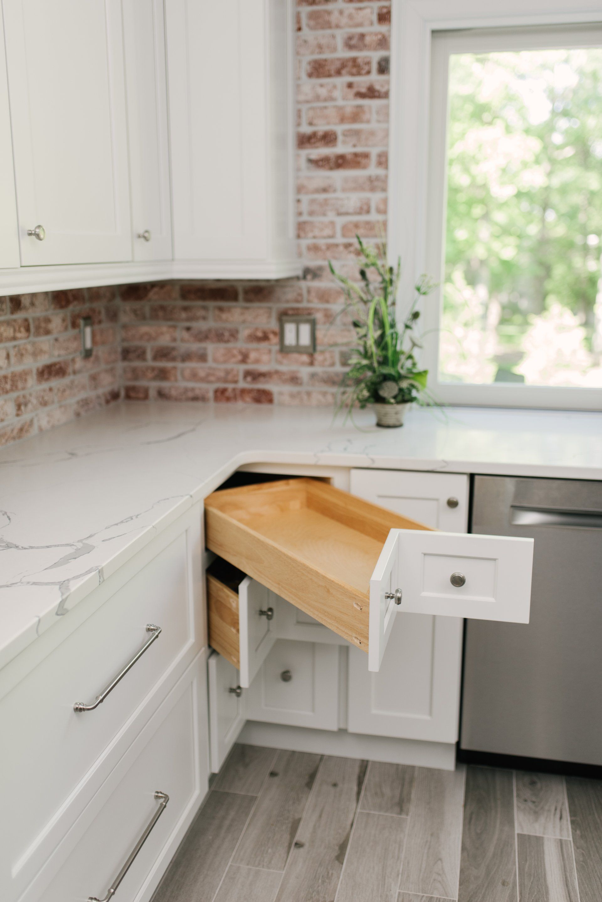 A kitchen with white cabinets and a wooden drawer open.