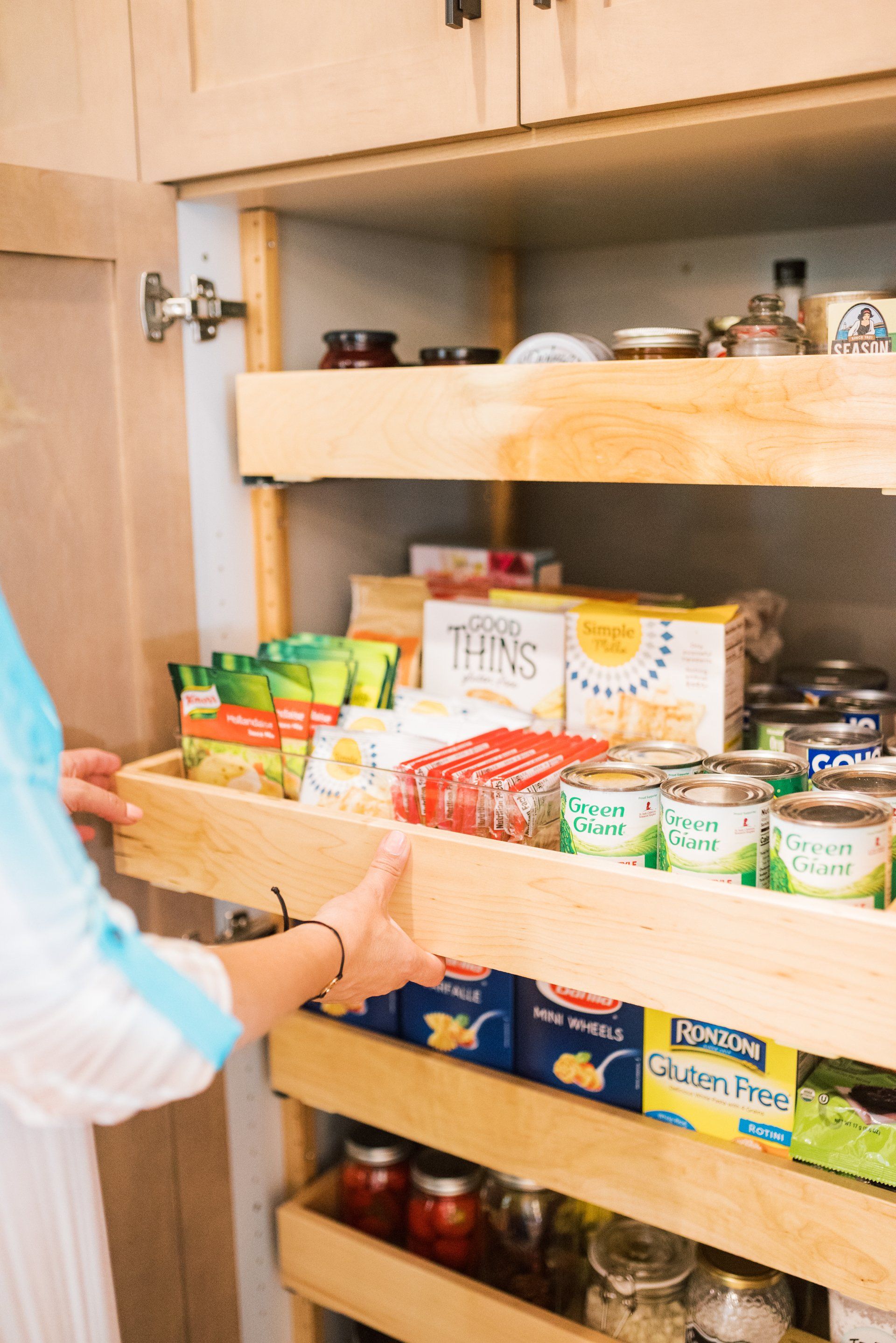 A person is pulling out a drawer in a pantry filled with food.