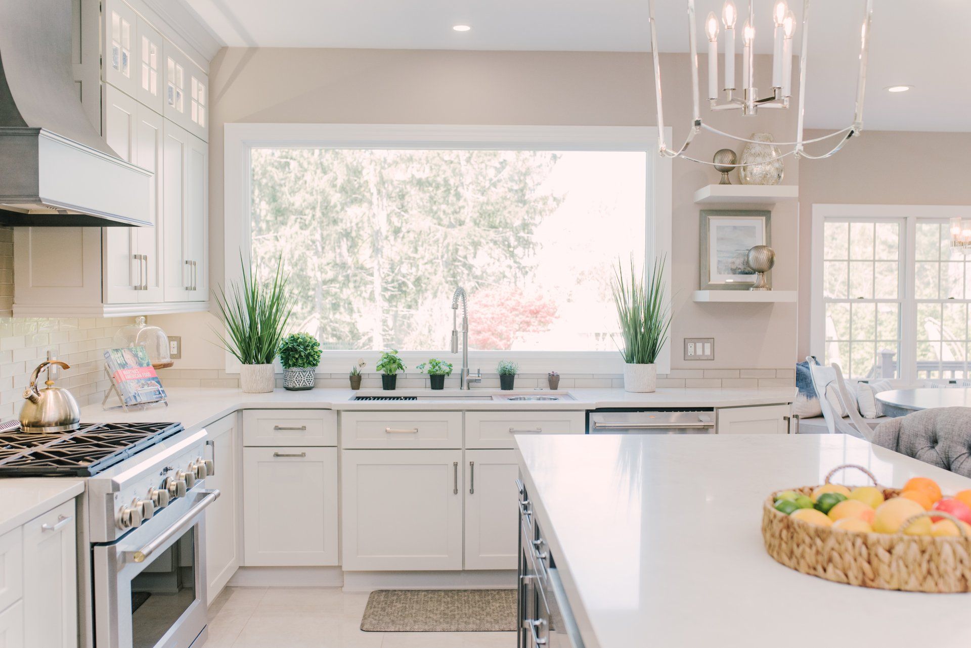 A kitchen with white cabinets , stainless steel appliances , a large island and a large window.