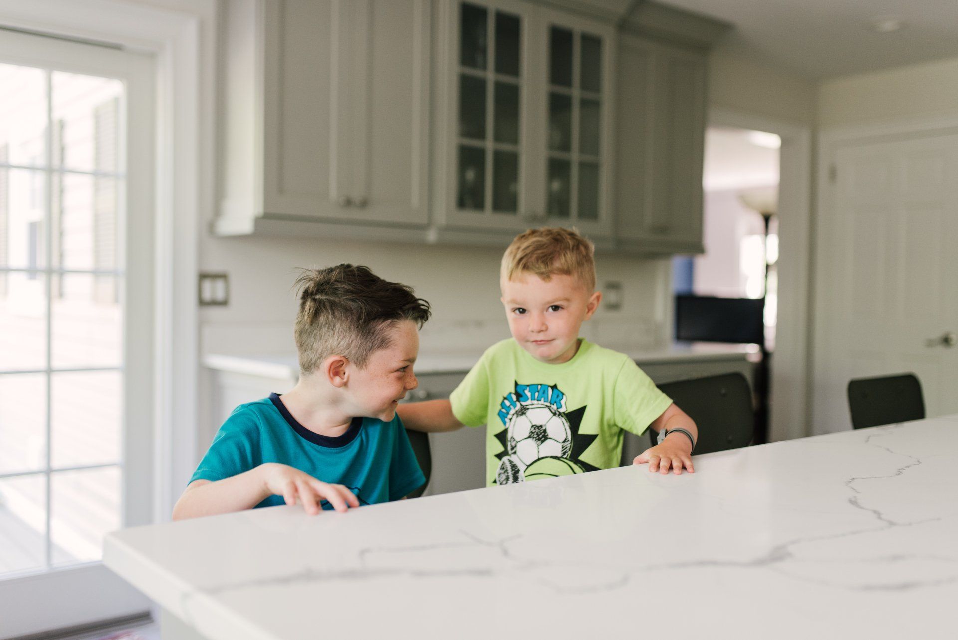 Two young boys are sitting at a counter in a kitchen.