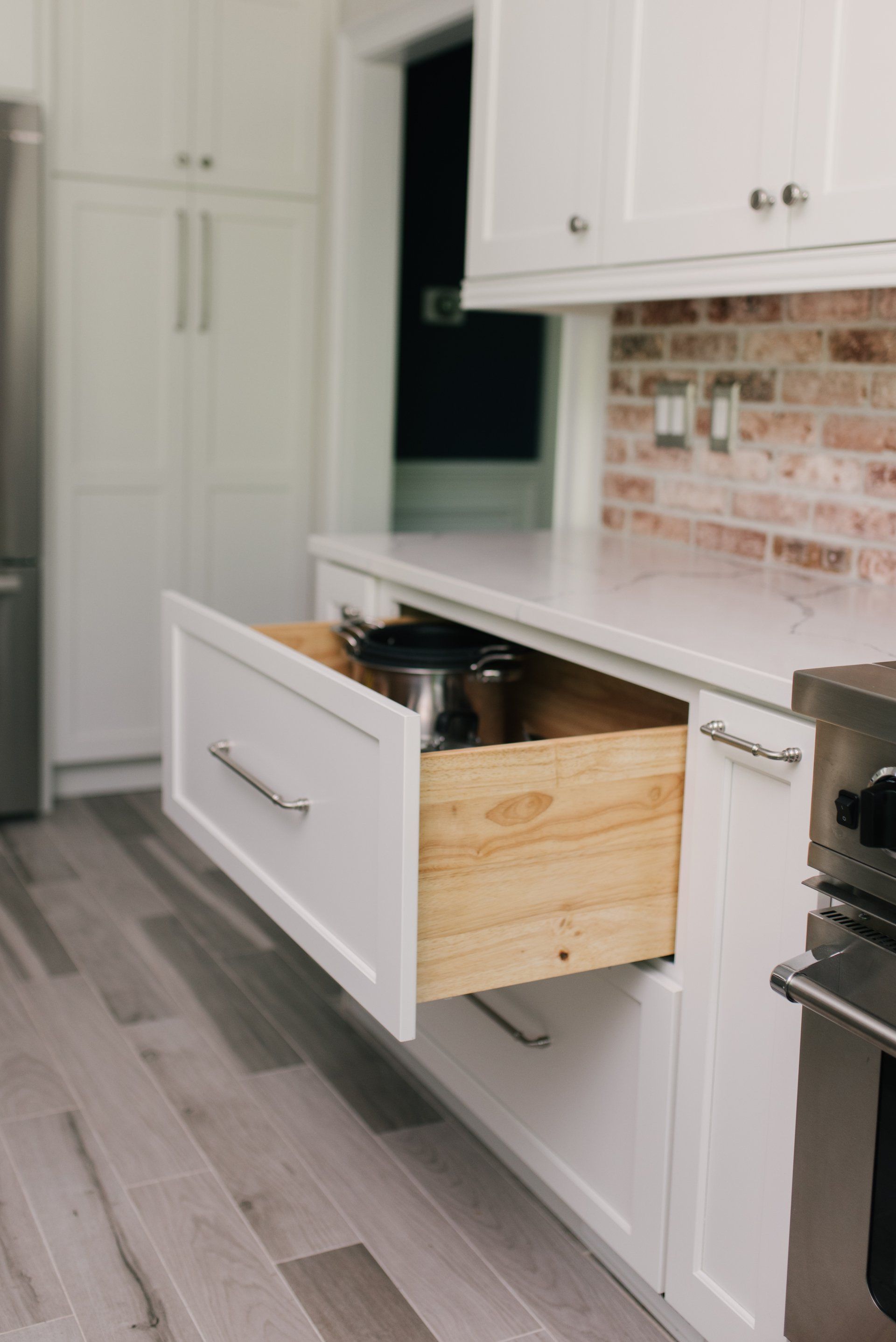 A kitchen with white cabinets and a wooden drawer open